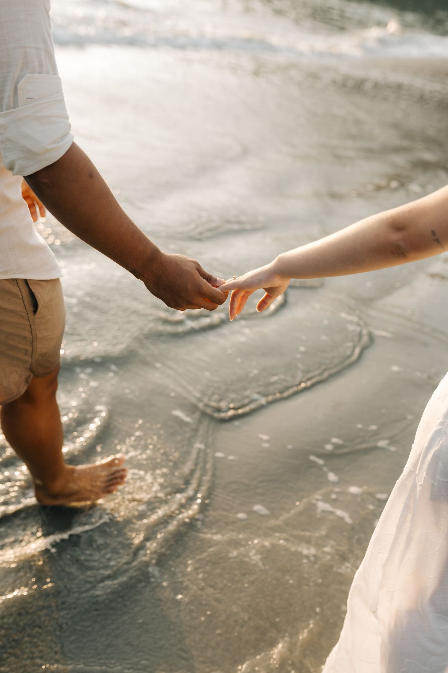 Close-up of hands clasped together while standing in shallow beach water.