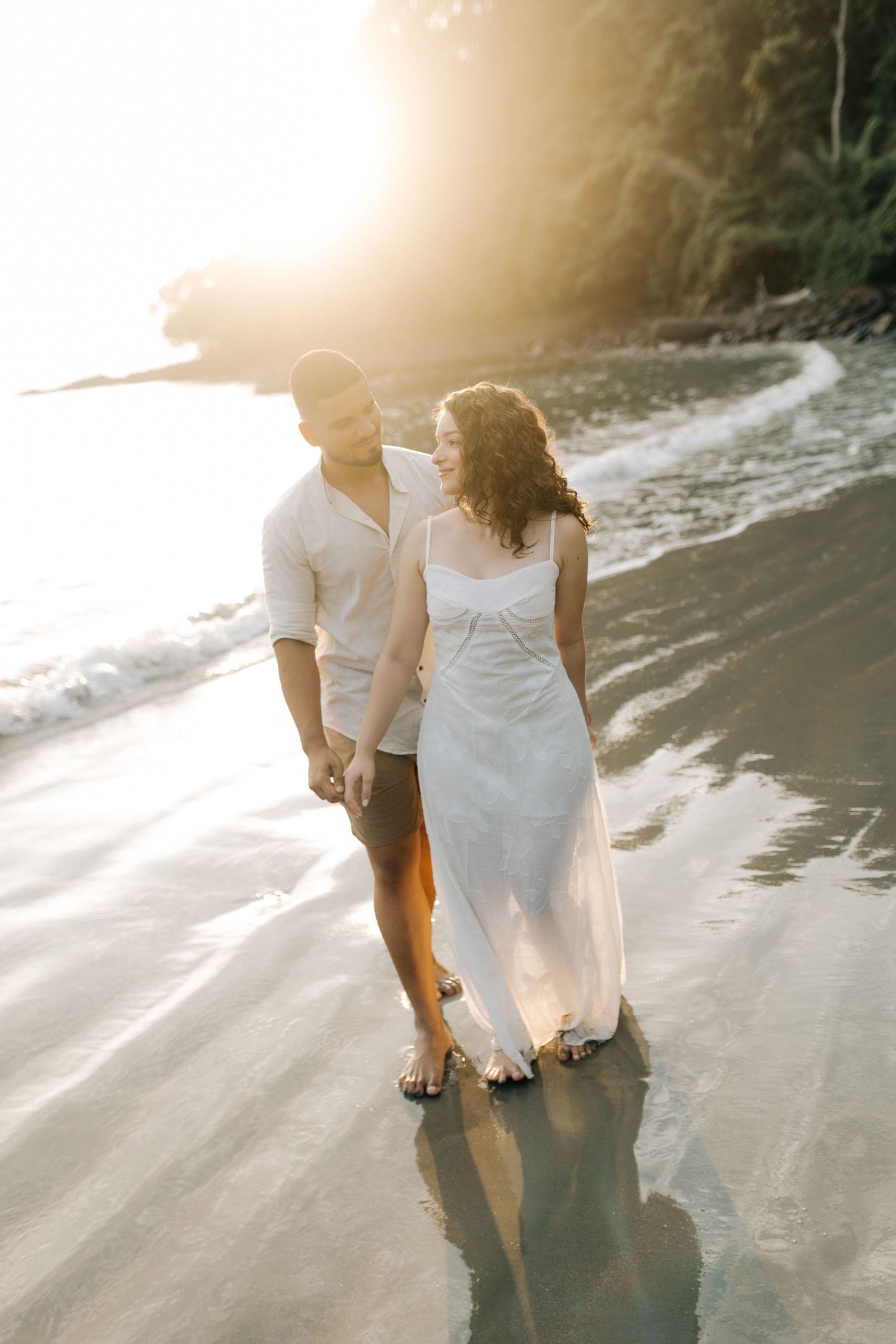 Couple walking together along the shoreline during sunset beach photoshoot.
