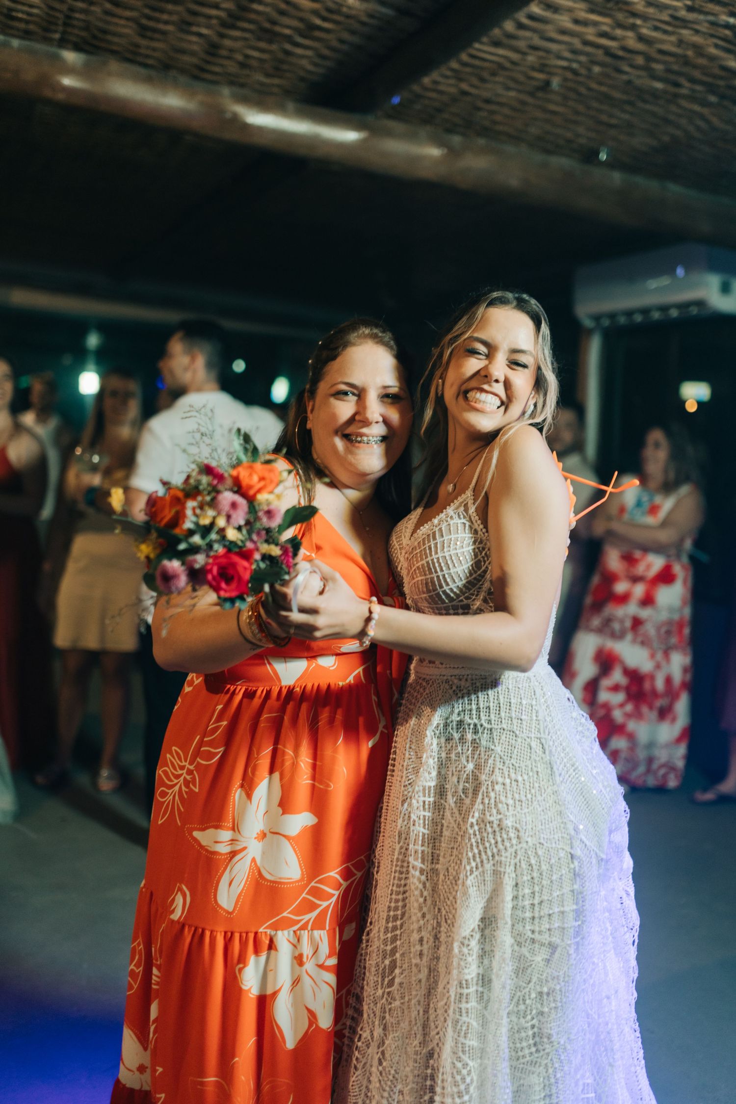Wedding guests in orange and white dresses share a joyful moment during the reception.