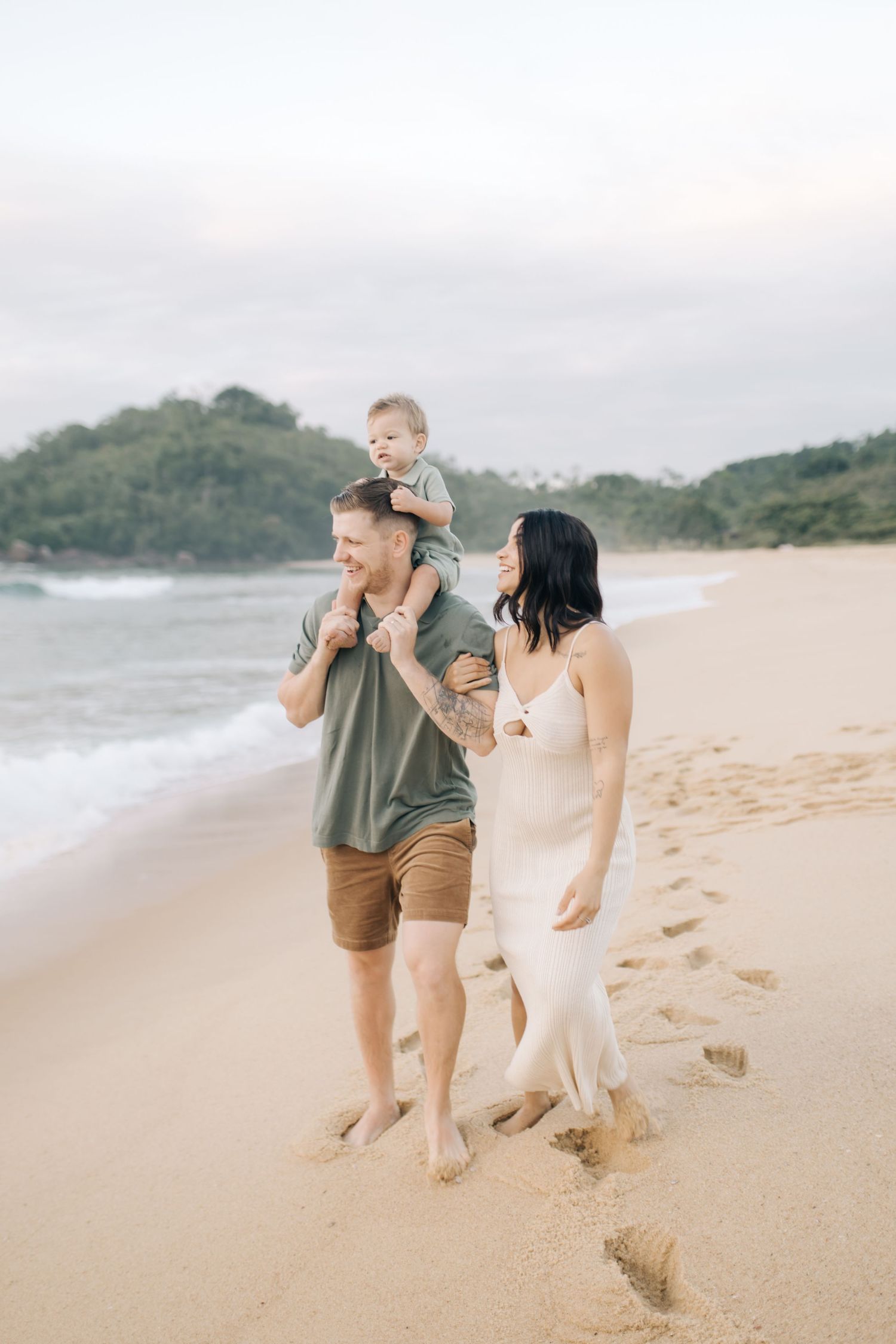 A family walks together along a scenic beach with green hills in the background.