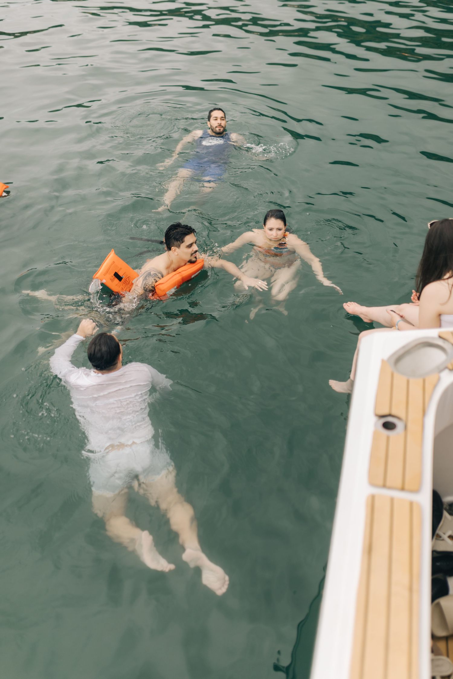 Group of people swimming in turquoise water next to a boat with wooden deck.