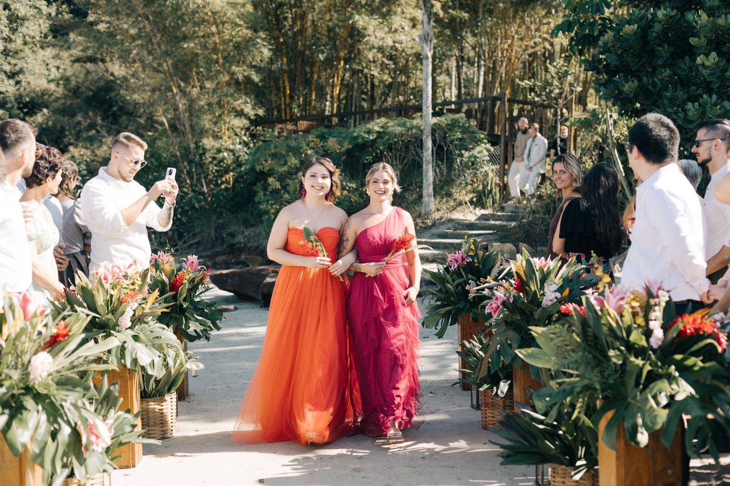 Outdoor wedding reception with guests in vibrant orange and burgundy attire.