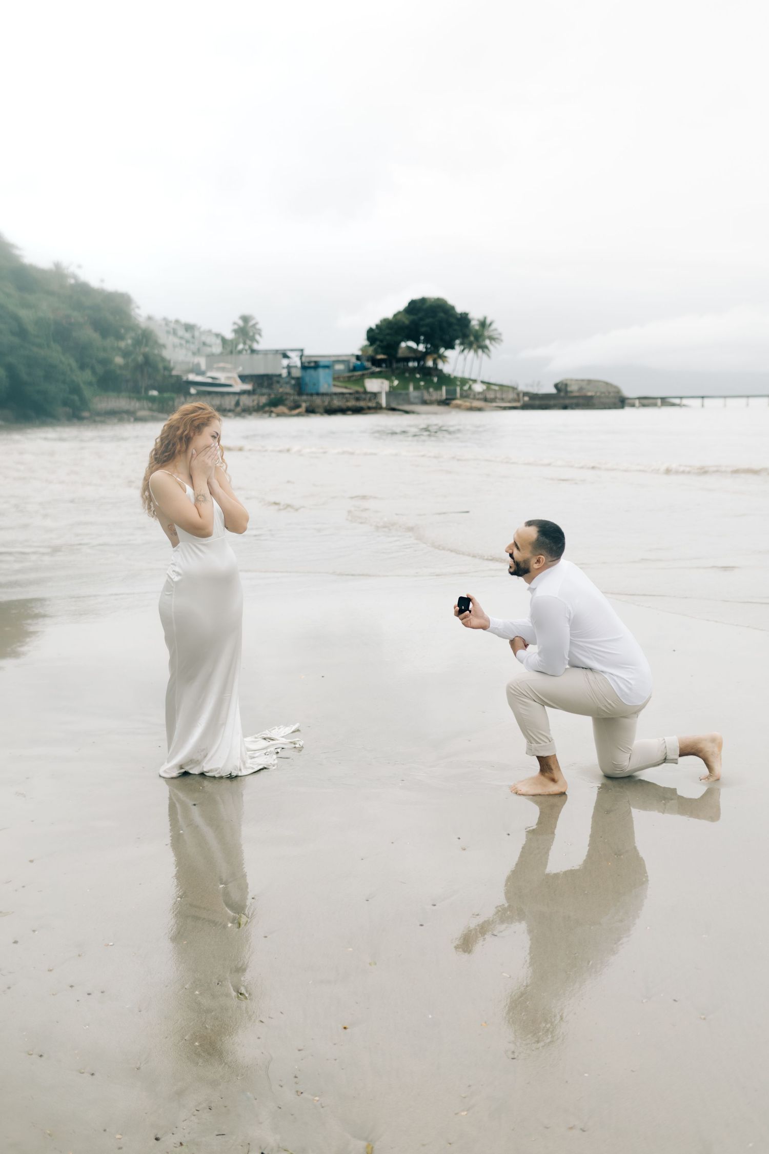 Emotional beach proposal moment captured with surprised reaction.