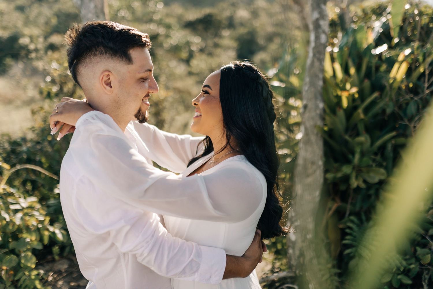 Couple sharing romantic moments among trees during a sunlit outdoor photoshoot.
