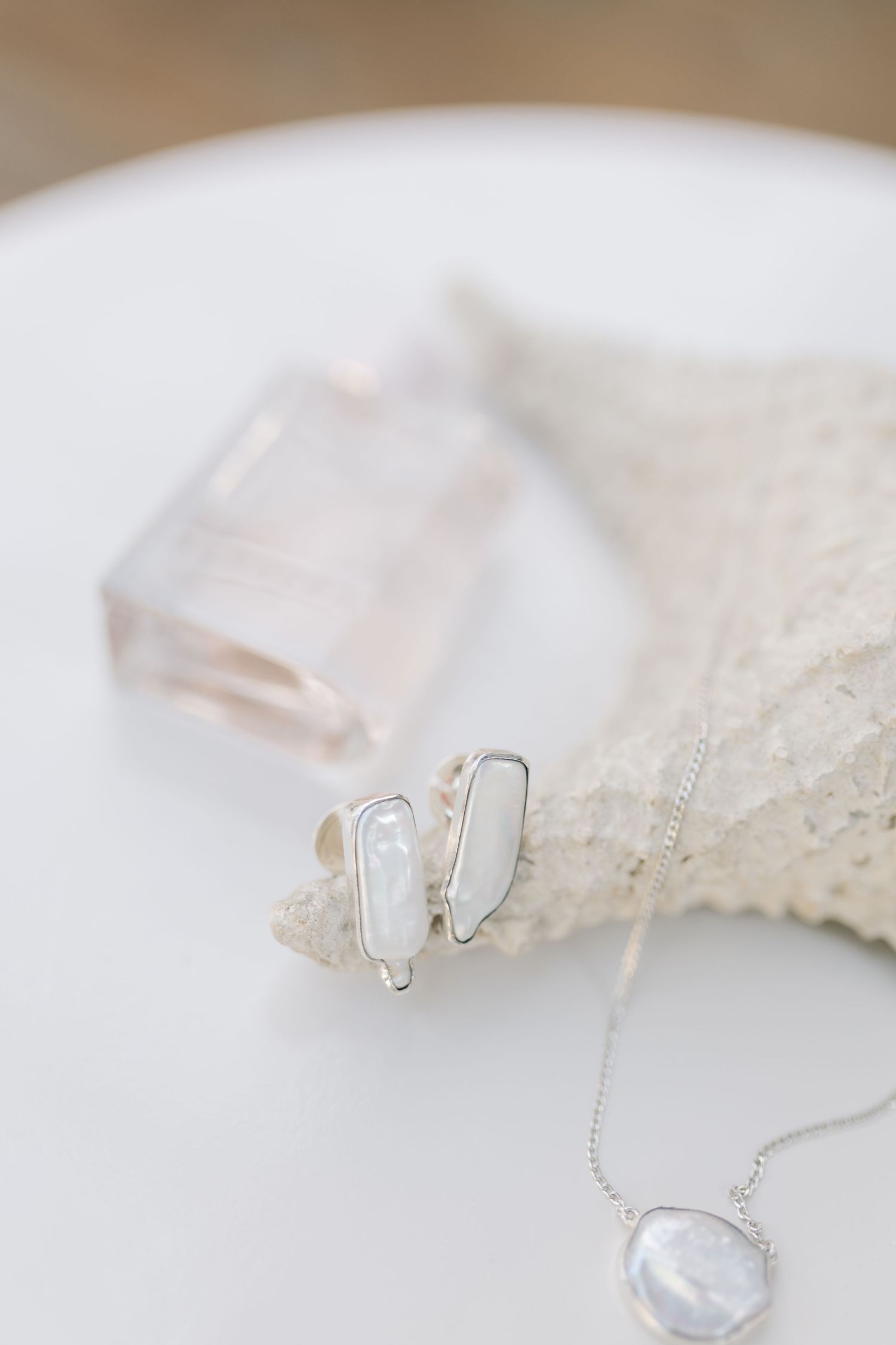 Pearl stud earrings and necklace arranged on white lace against a light background.
