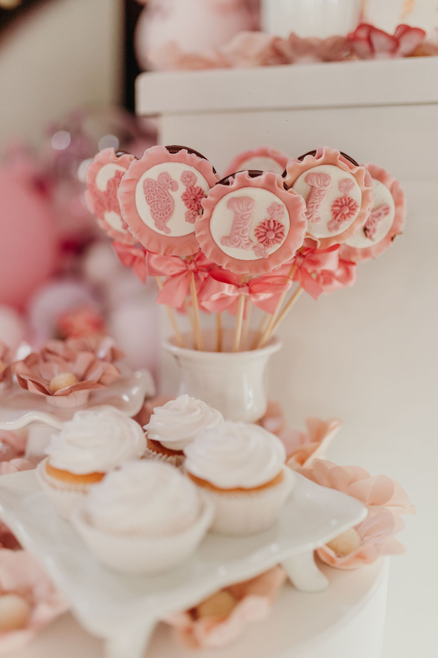 Pink cake pops and frosted cupcakes arranged on a white dessert display.