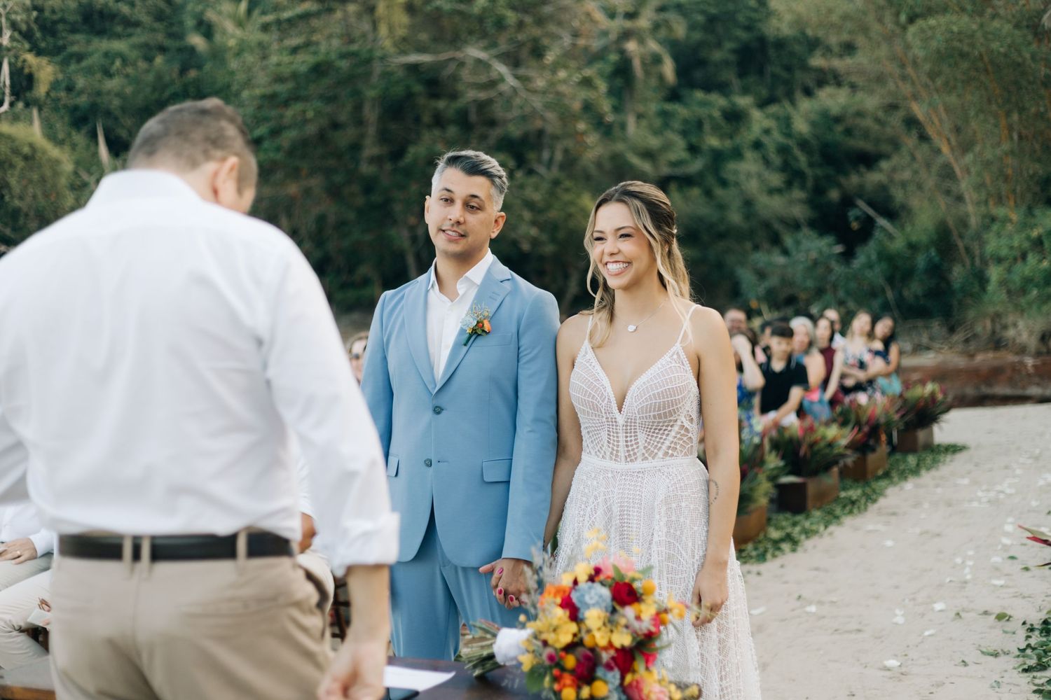 Intimate beachside wedding ceremony with blue suit and white dress.
