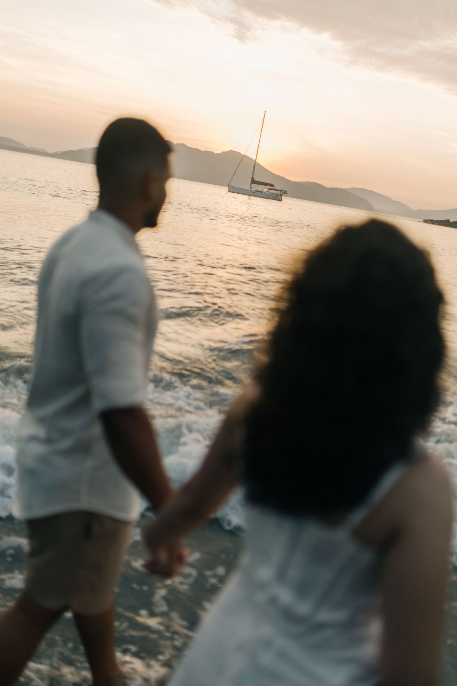 Silhouetted figures walking hand in hand along the beach at sunset.