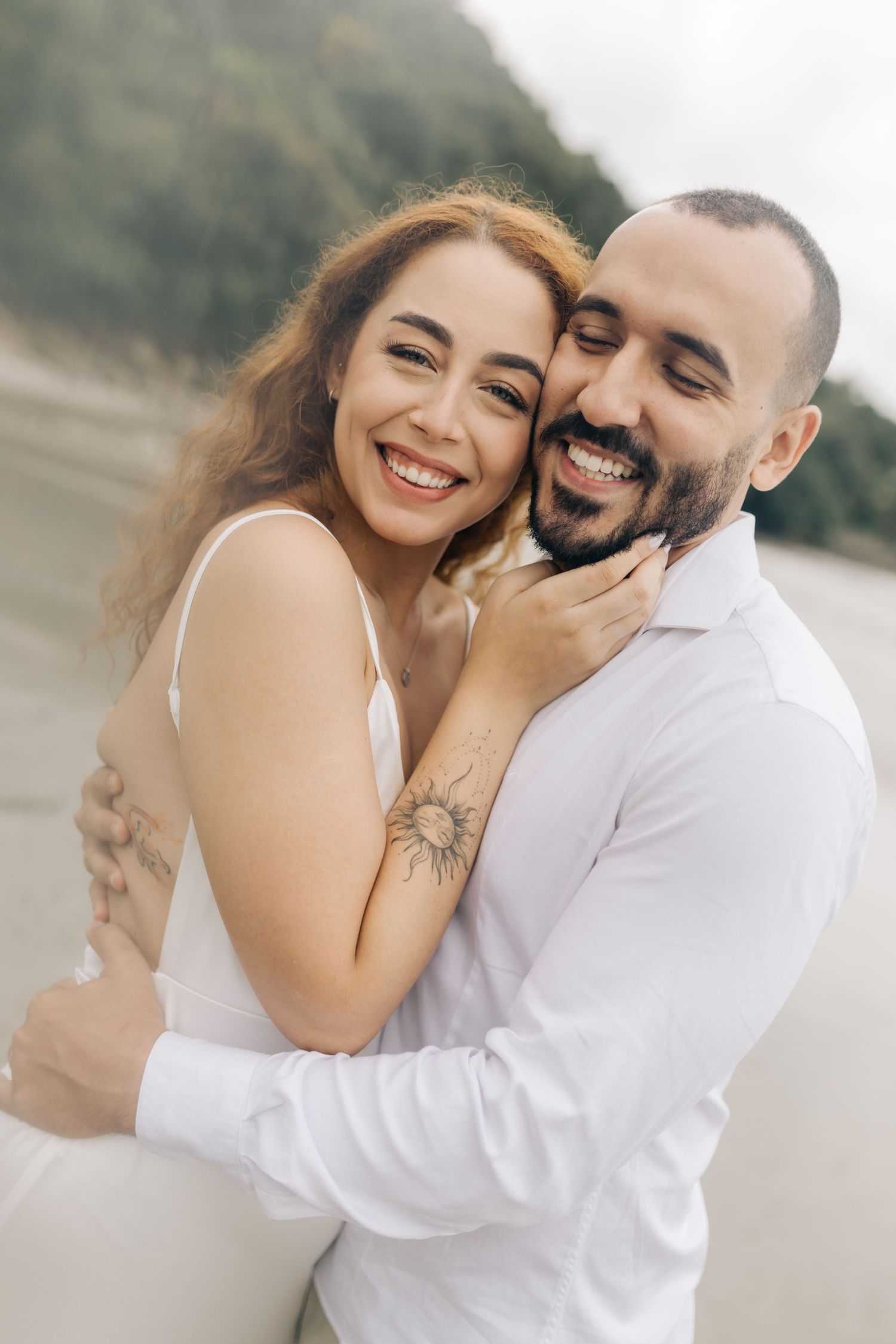 Joyful couple sharing intimate moments during a beach photoshoot with soft lighting.