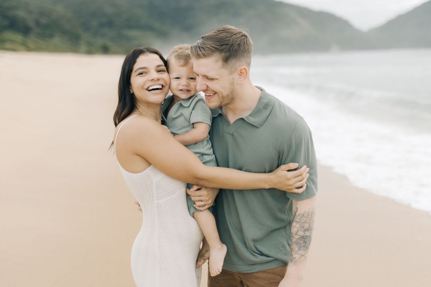 A family shares tender moments on a beautiful beach with mountains in the background.