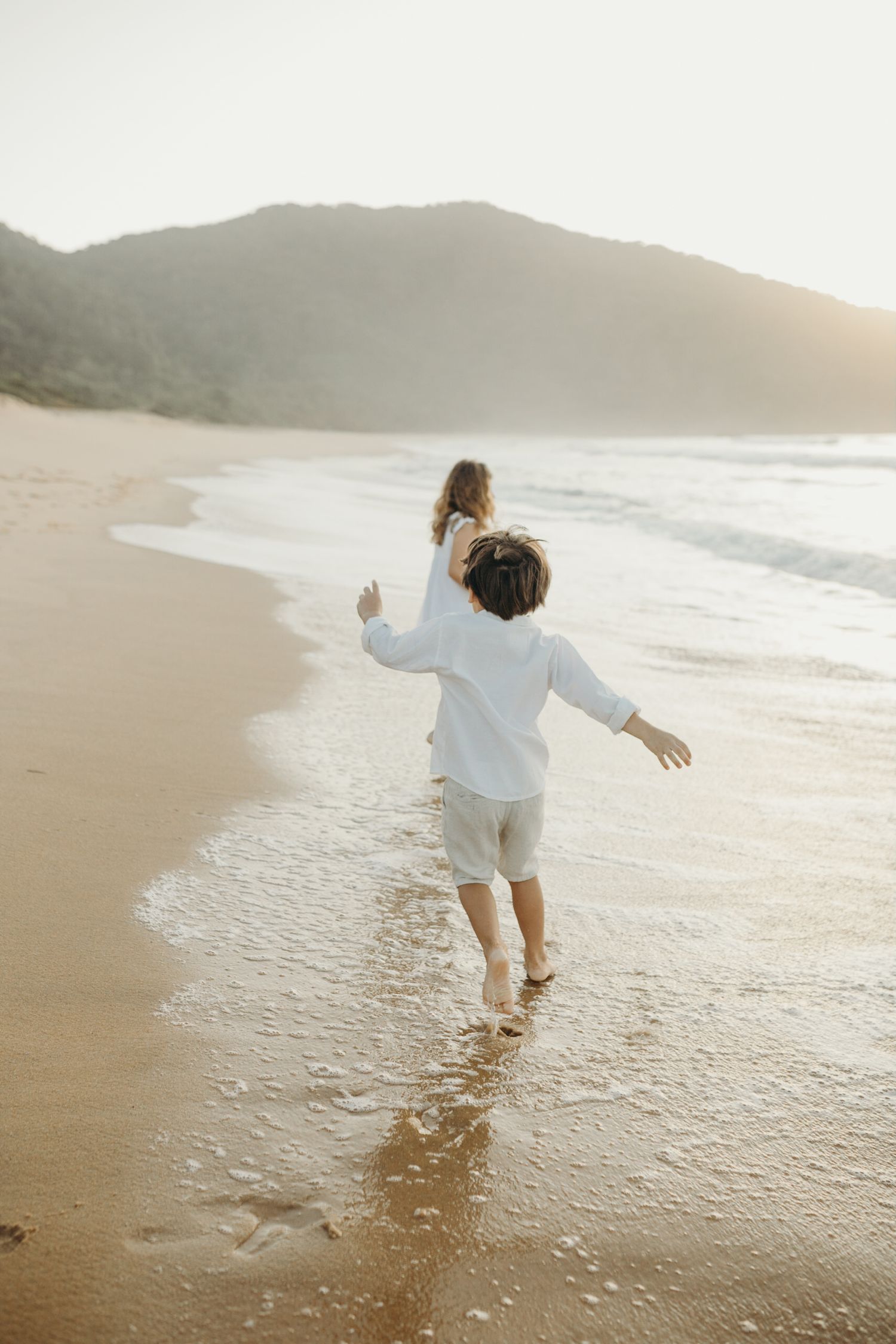 People in white clothing splashing and playing in shallow ocean water at sunset.