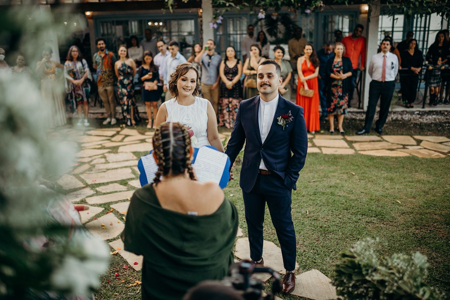 Outdoor wedding celebration with guests gathered on a manicured lawn near stone pathways.