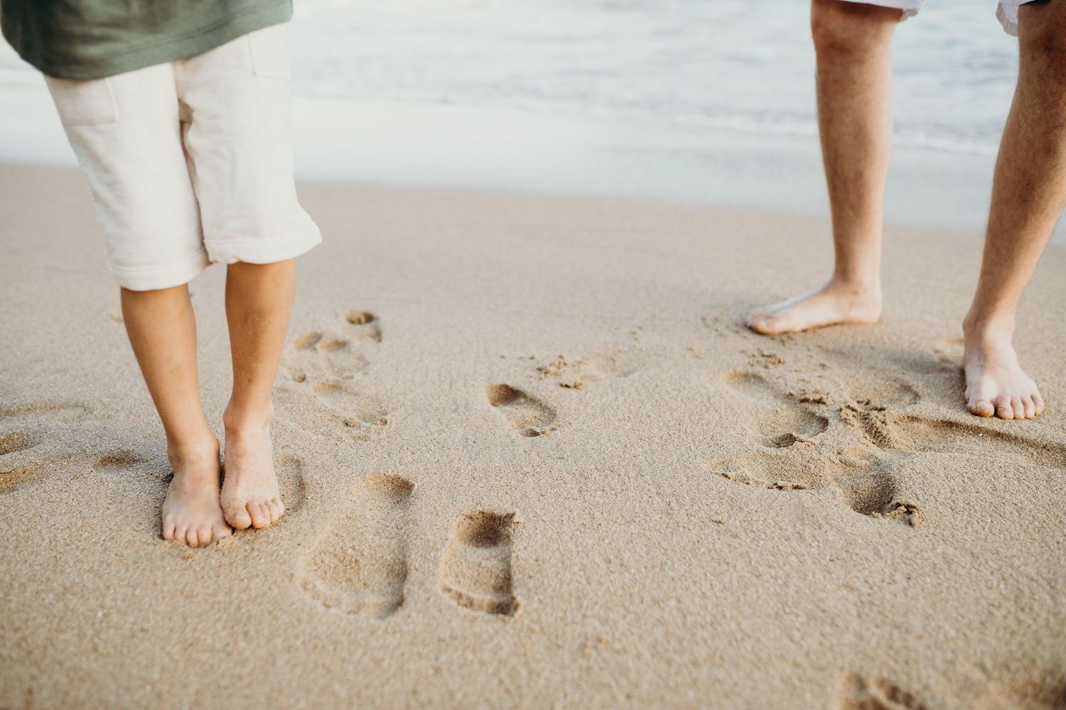 Bare feet making footprints in wet sand on a beach shoreline.