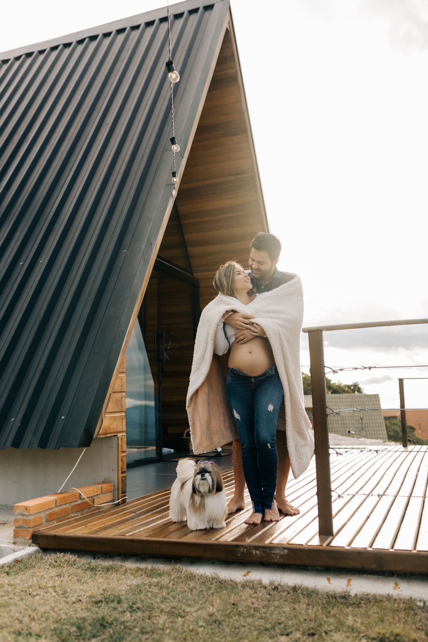 Sweet maternity photos captured on a wooden deck of an A-frame cabin during sunset.