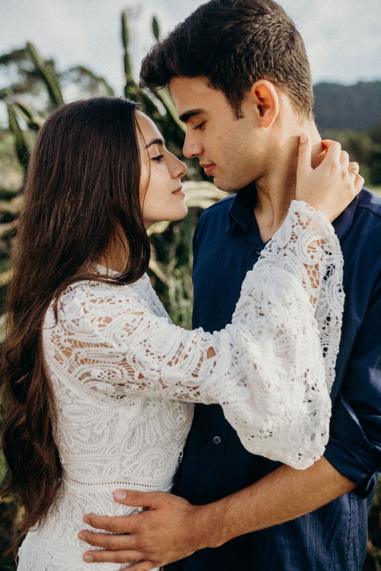A romantic embrace between a couple wearing white lace and navy blue against a natural backdrop.