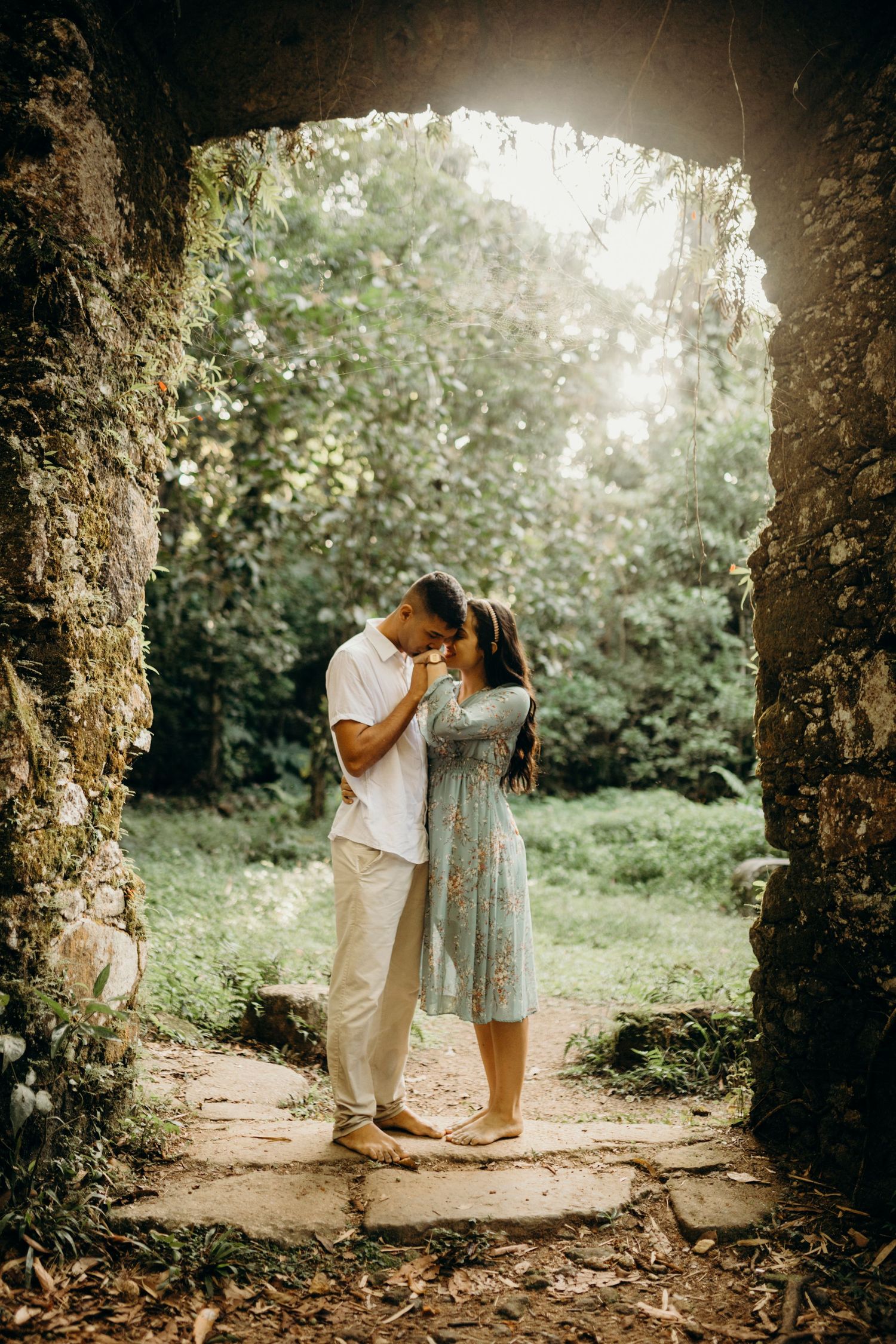Couple sharing a tender moment under a stone archway in a lush garden setting.
