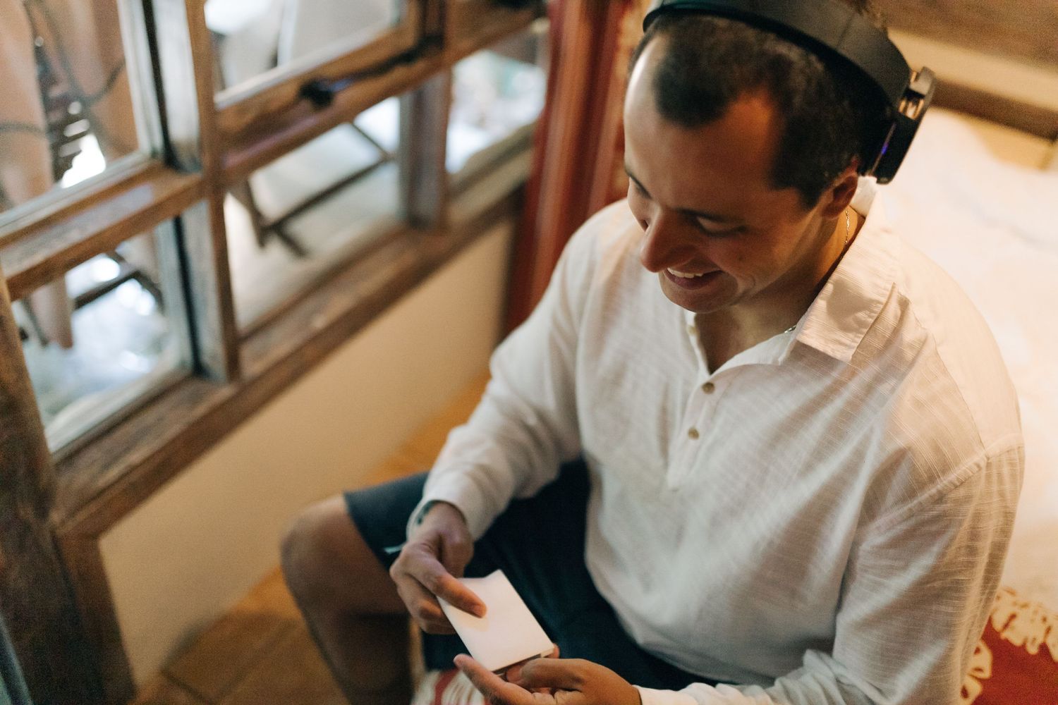 A person in a white polo shirt sits and reads while wearing headphones.