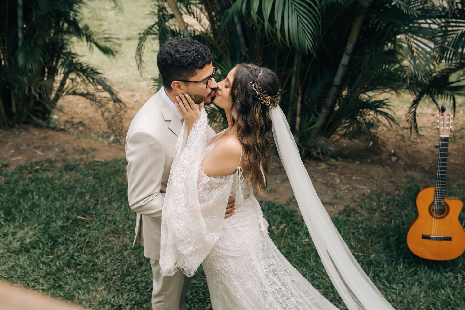 A romantic couple embraces during their wedding photoshoot in a lush garden with a guitar in background.
