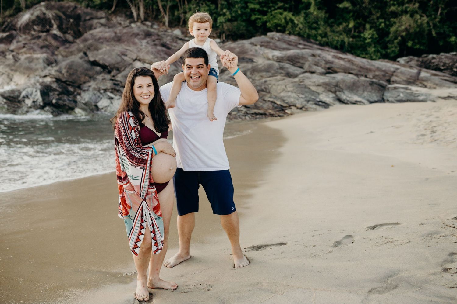 Family enjoying a sunny day at a secluded beach surrounded by rocks and tropical vegetation.