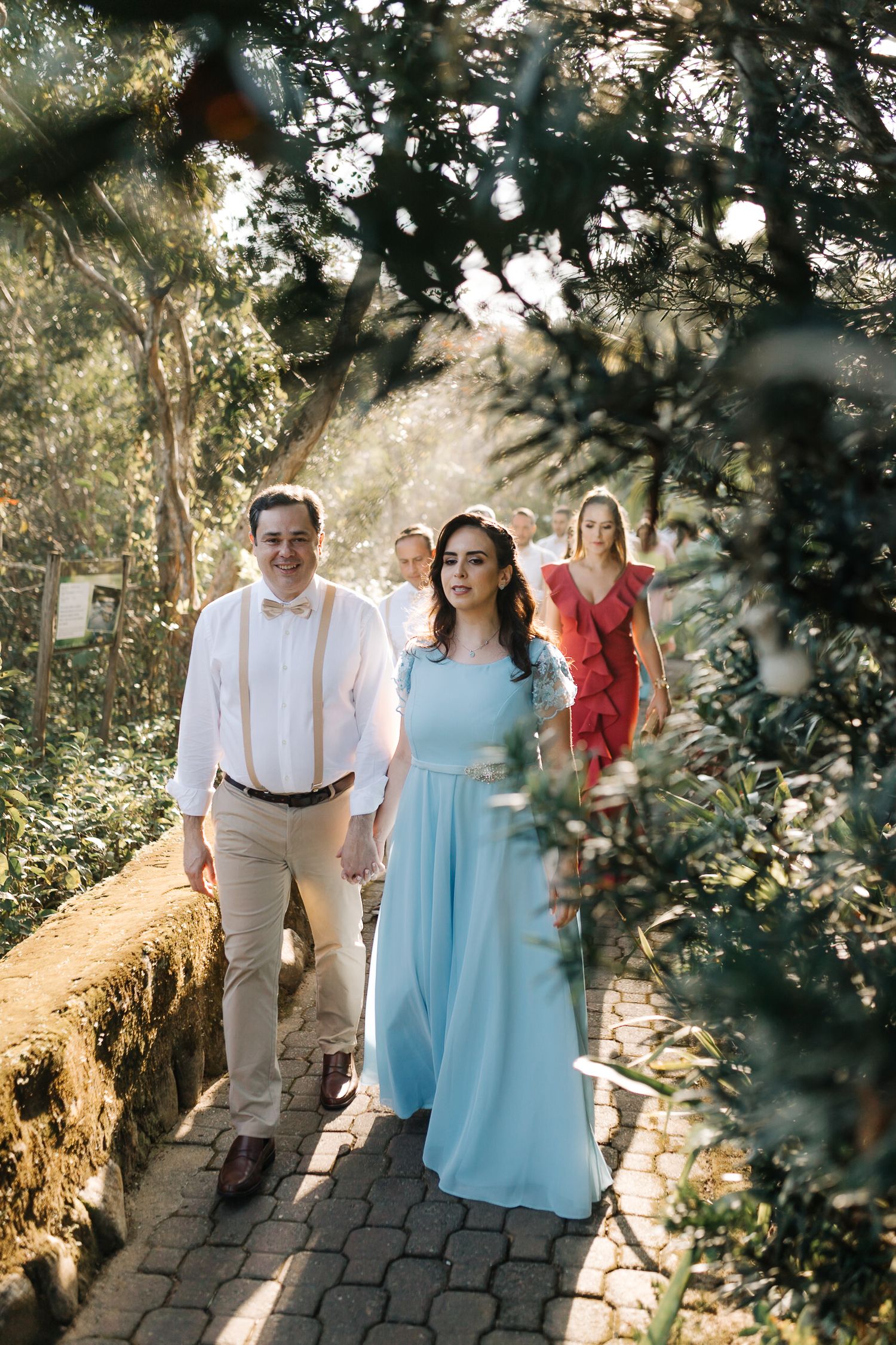 Wedding party walking along a scenic garden path in formal attire.