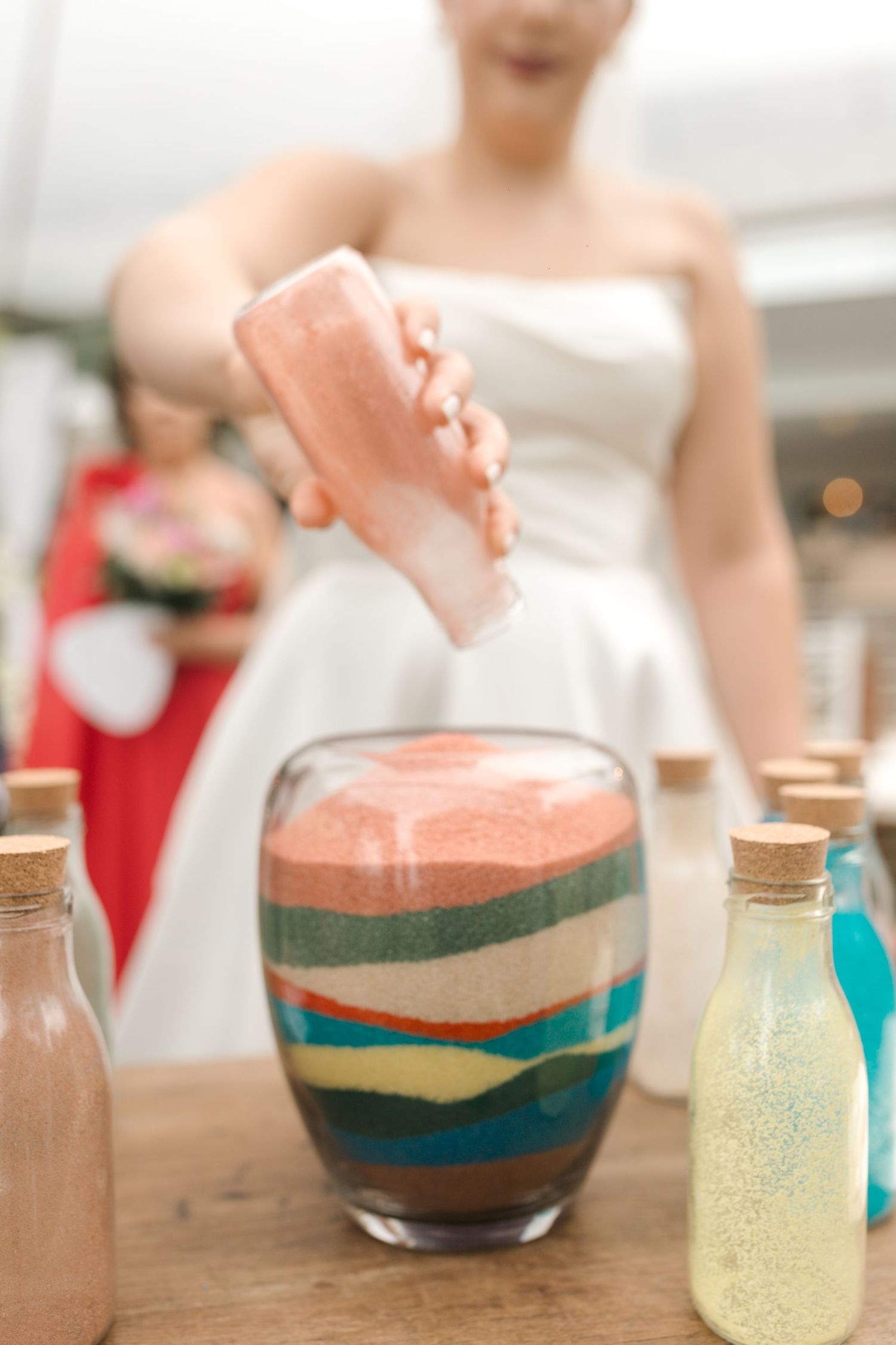 Layered colorful sand being poured into decorative glass vessel during wedding ceremony.