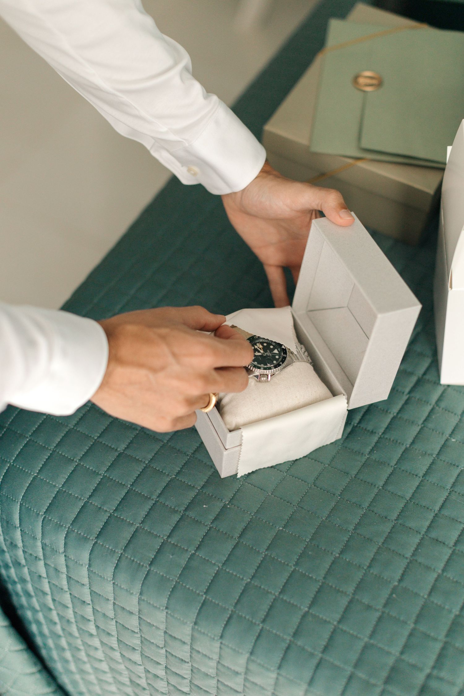 Opening a luxury watch box revealing a dark timepiece against green quilted fabric.