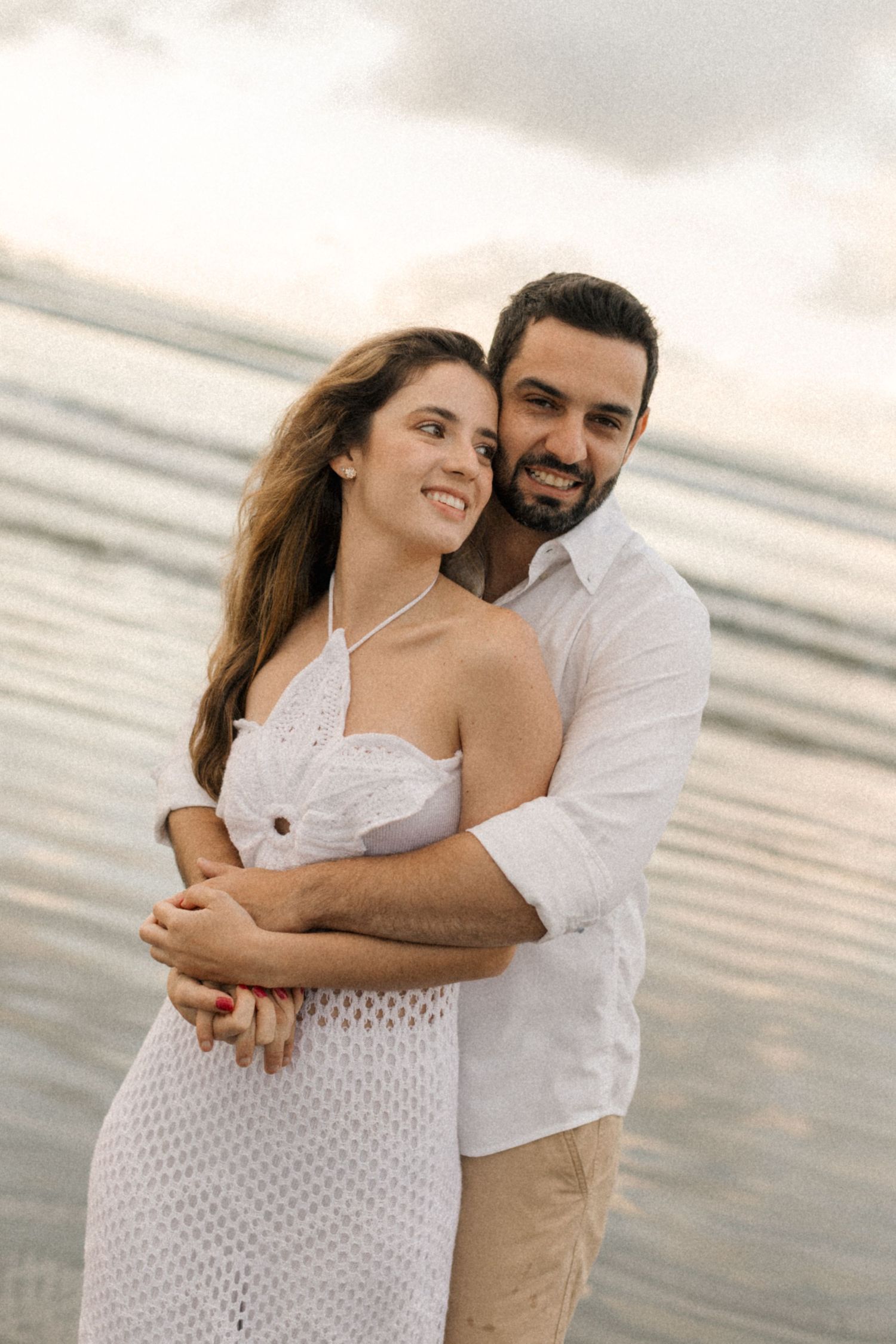 Loving couple sharing intimate moment on beach with ocean waves and sunset behind them.