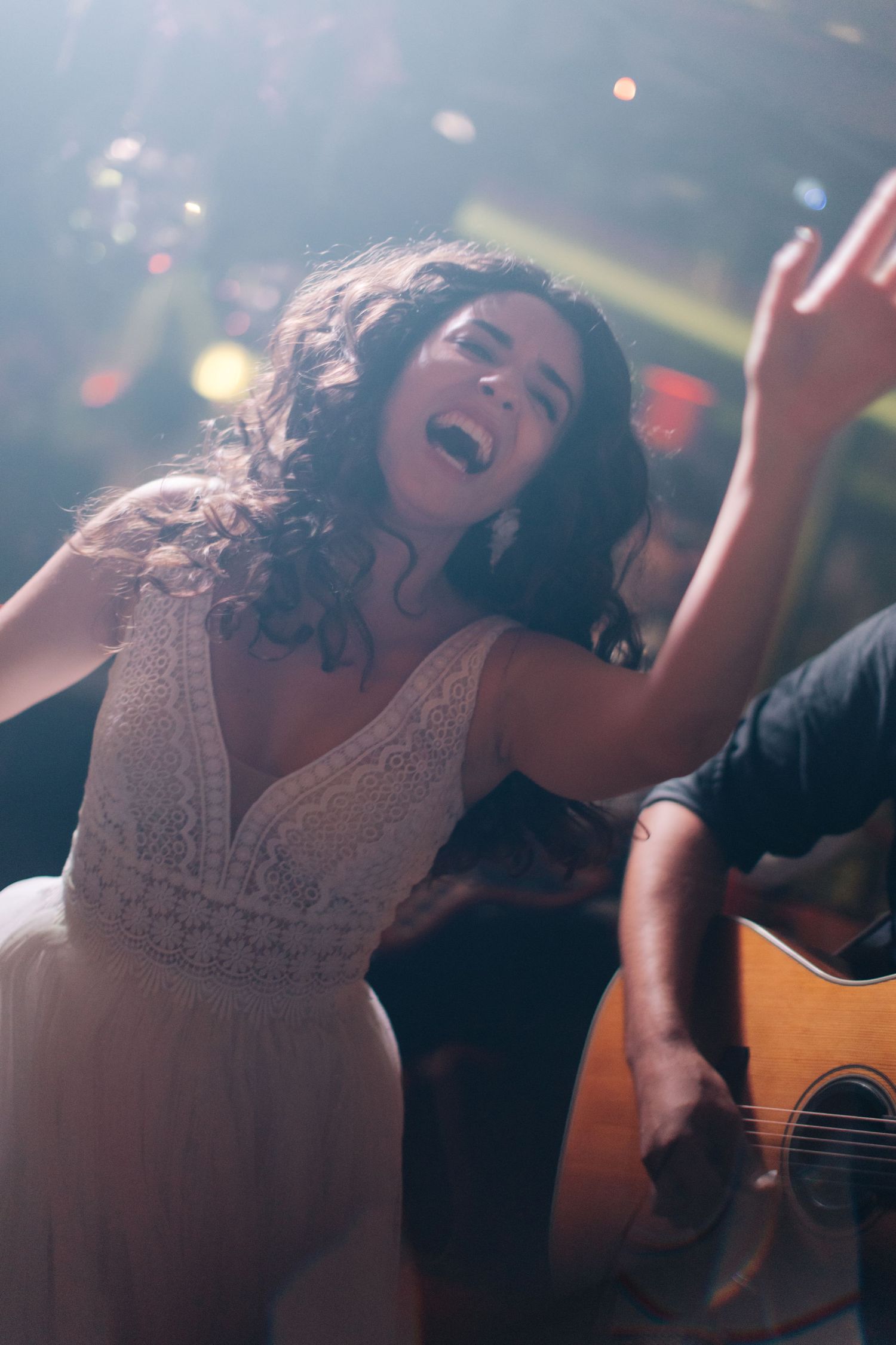 Singer in white lace dress performs passionately with live band at intimate venue.