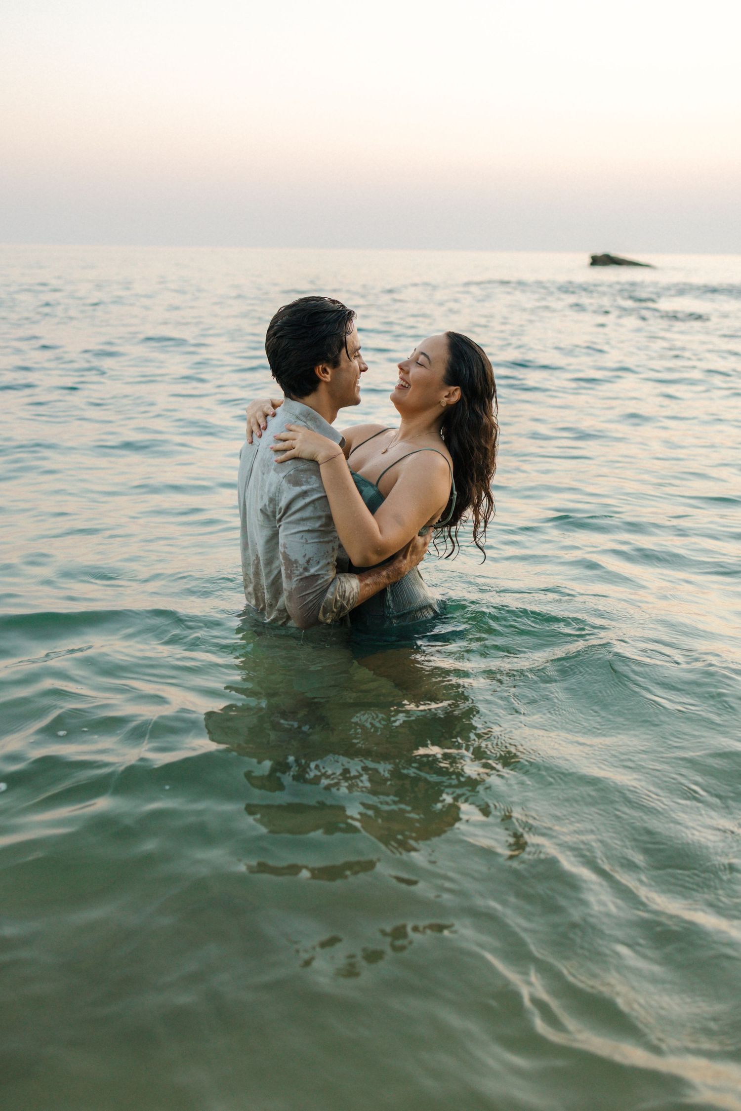 Couple embracing in ocean waters during sunset with calm seas in background.