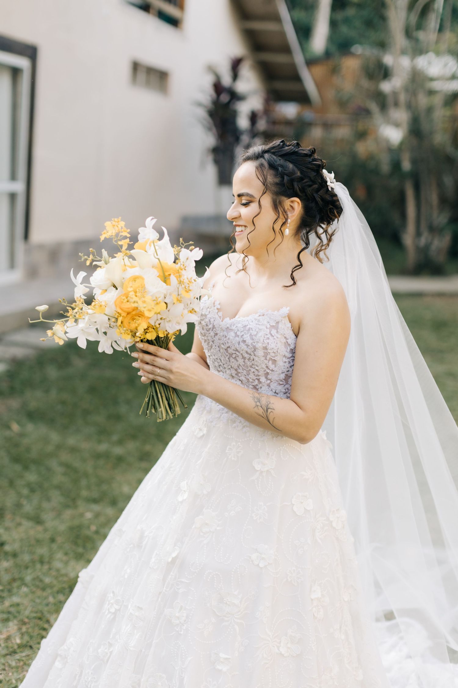 An elegant white lace wedding gown with a flowing veil and vibrant yellow bouquet.