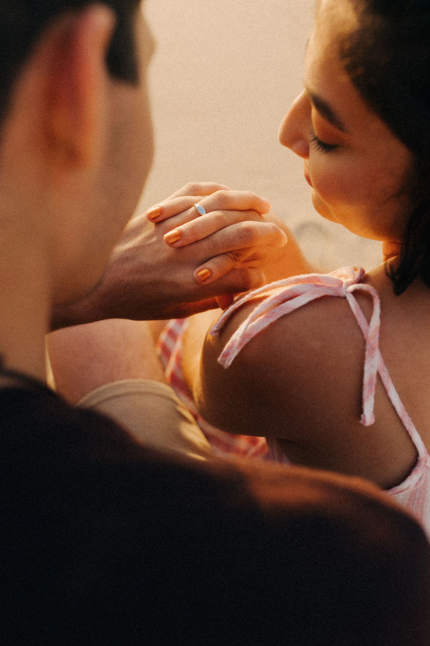 An intimate moment between two people holding hands in warm sunlight, with soft focus and pink clothing details.Um momento íntimo entre duas