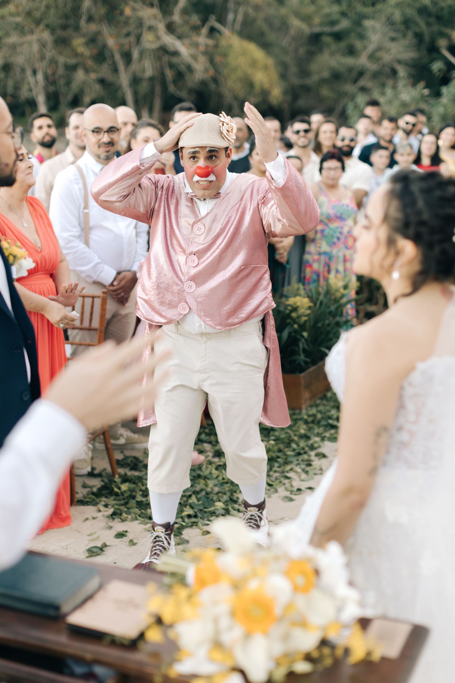 Guest in pink shirt and white pants performs energetic dance moves during wedding celebration.