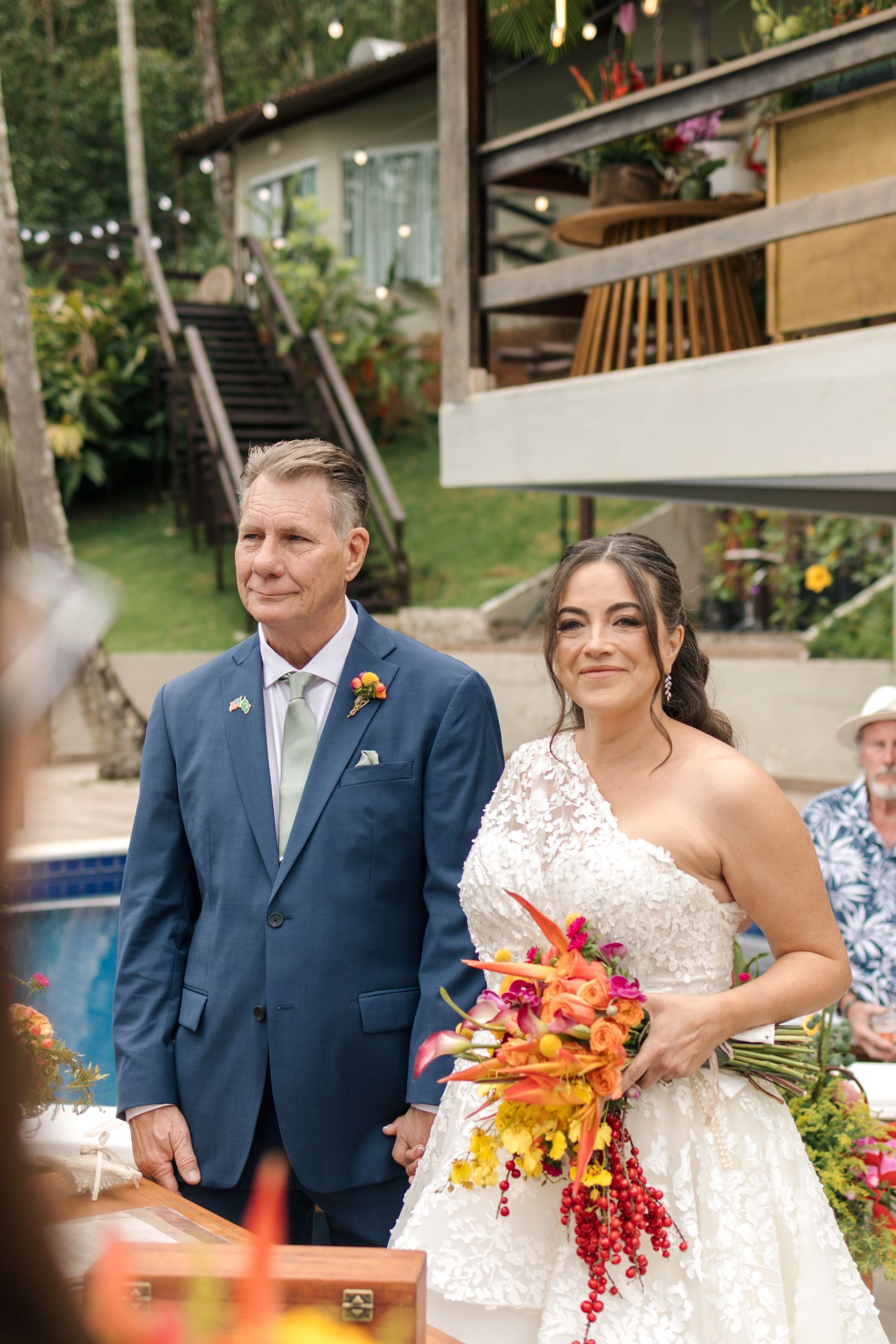 A tropical wedding ceremony with vibrant orange and red floral bouquets against a lush garden backdrop.