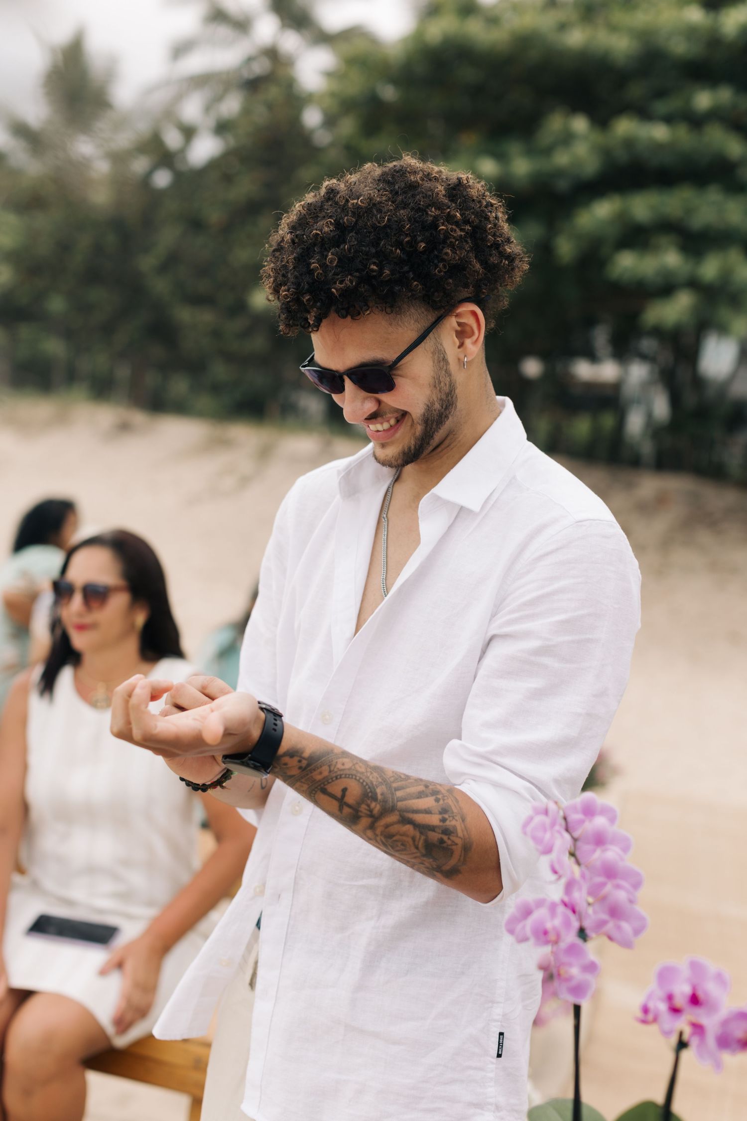 Guest in white linen shirt enjoying a beach wedding celebration with tropical flowers.