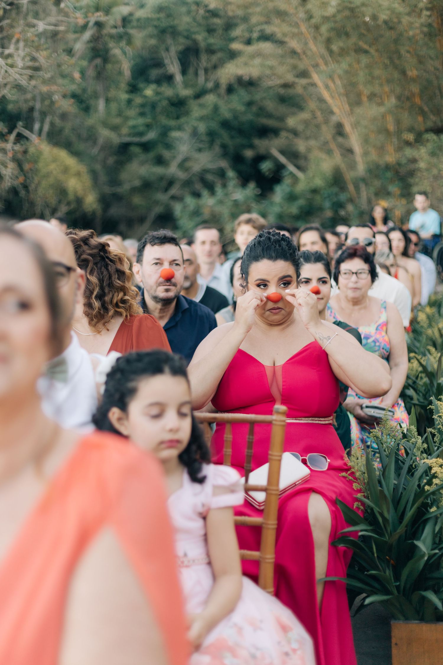 Wedding party wearing festive red noses and colorful dresses during outdoor celebration.