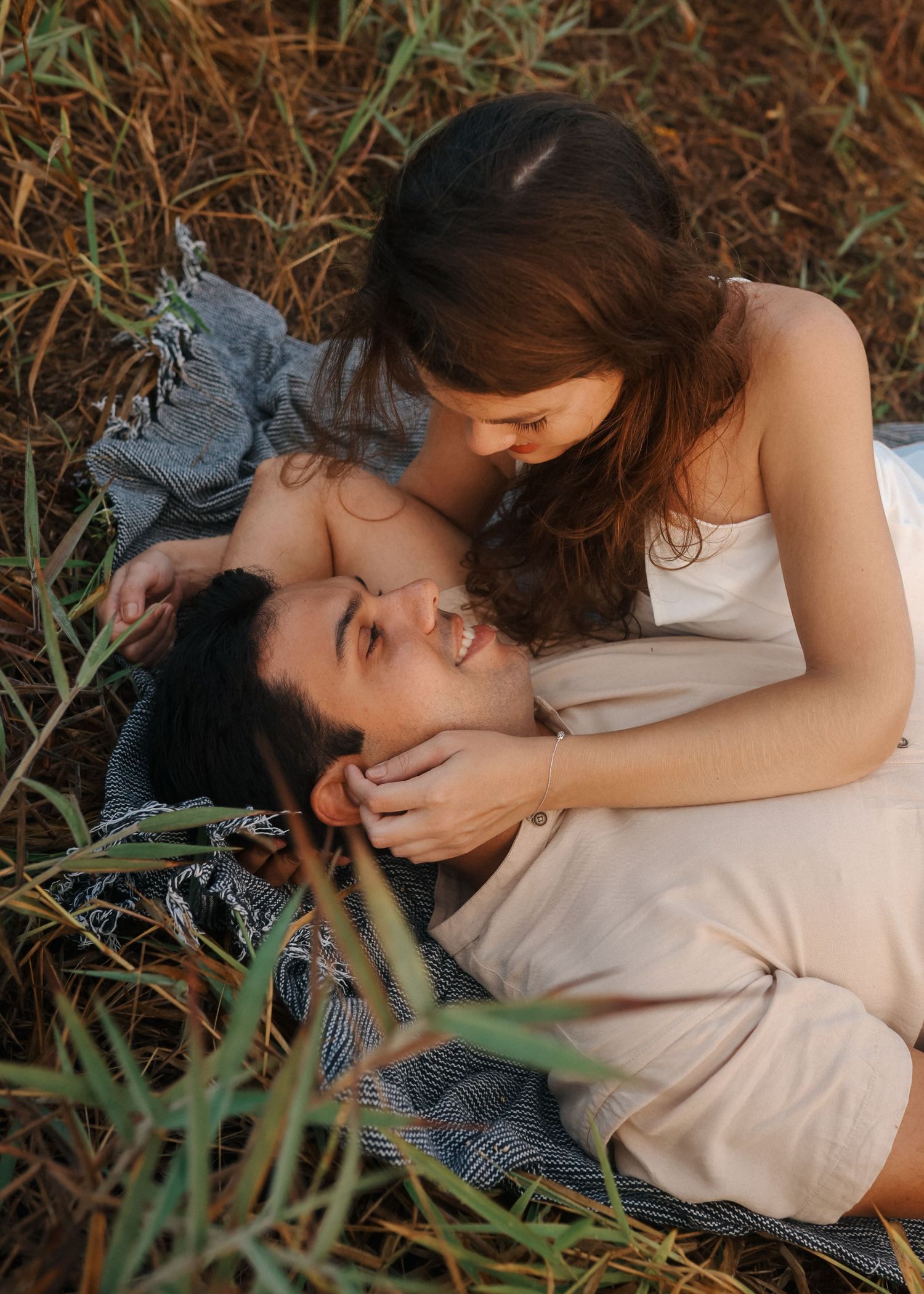 Intimate couple moment captured through tall grass during outdoor photo session.