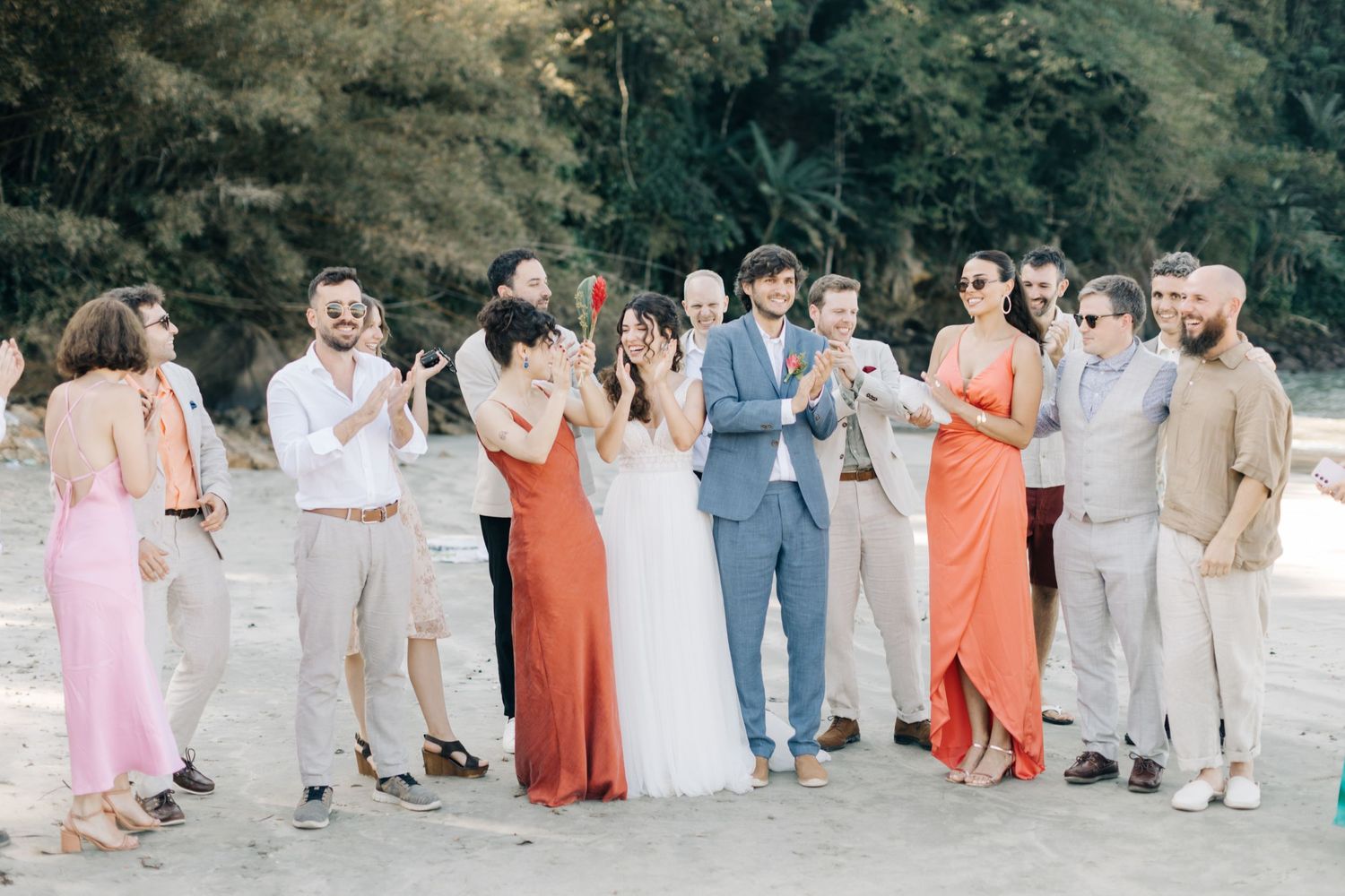 Wedding party members in coordinated coral and pastel dresses gather for a group photo.