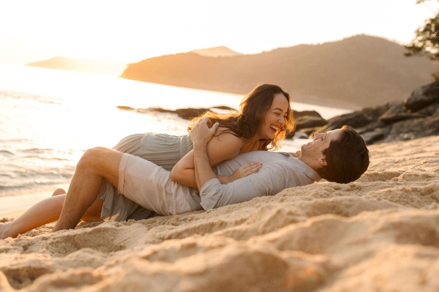 Elegant figure in white dress lying gracefully on sandy beach at sunset.