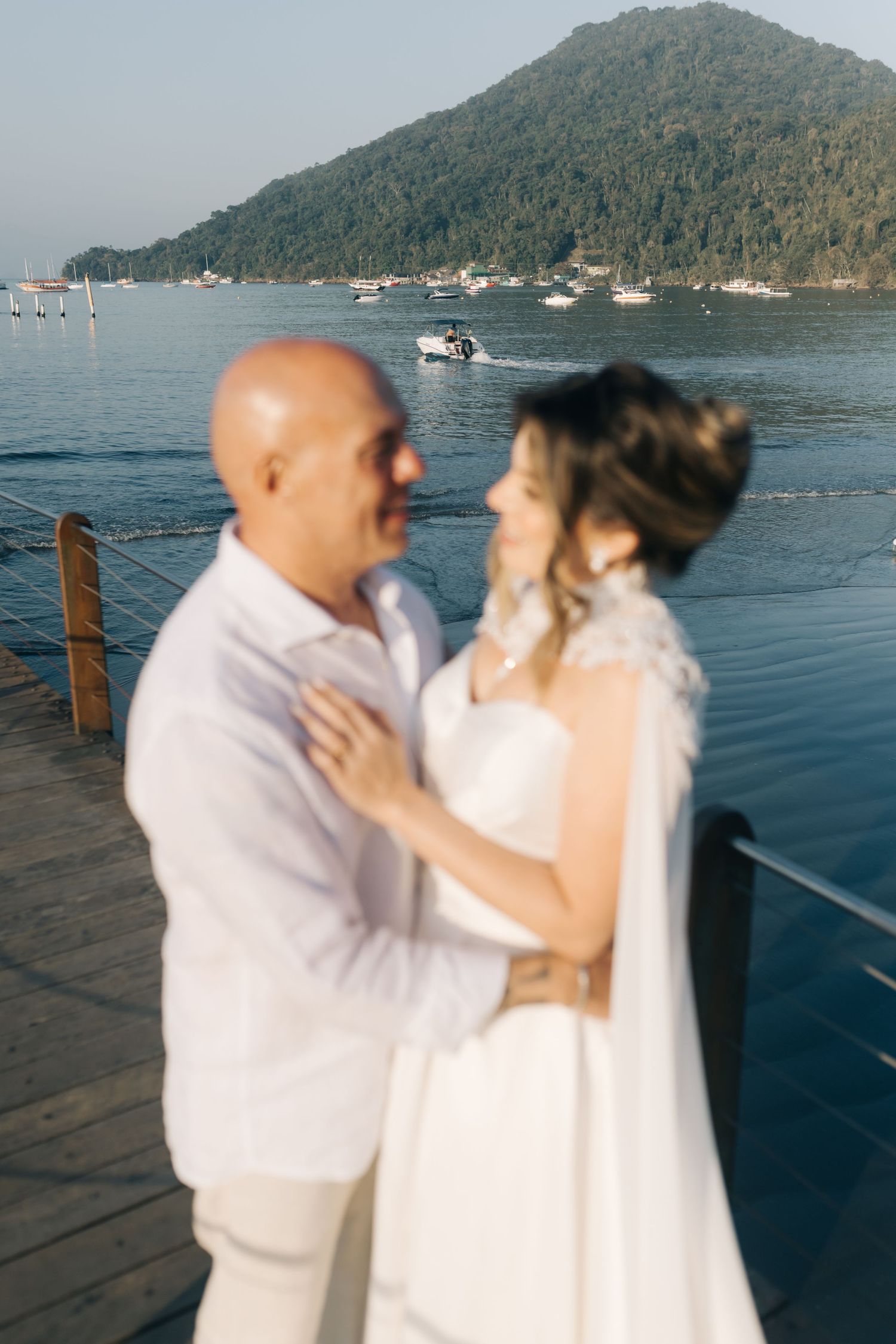 A romantic seaside moment between newlyweds with boats and mountains in the distance.