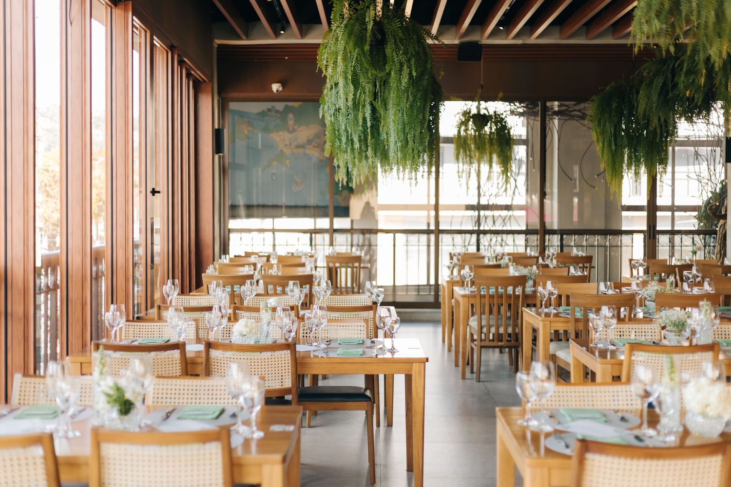 Modern restaurant interior with wooden tables and hanging plants from the ceiling.