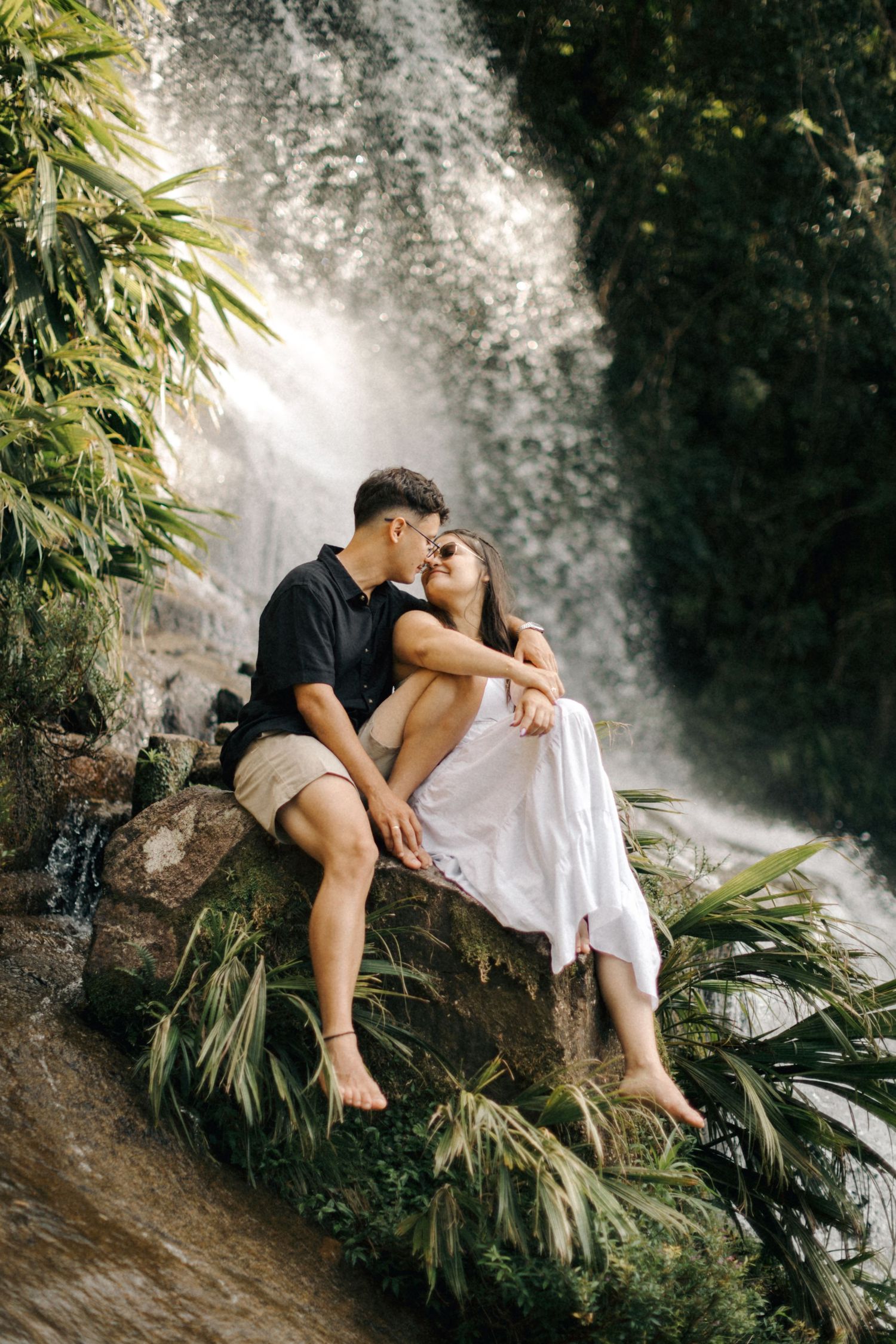 Romantic moment captured against the backdrop of a misty waterfall and tropical plants.