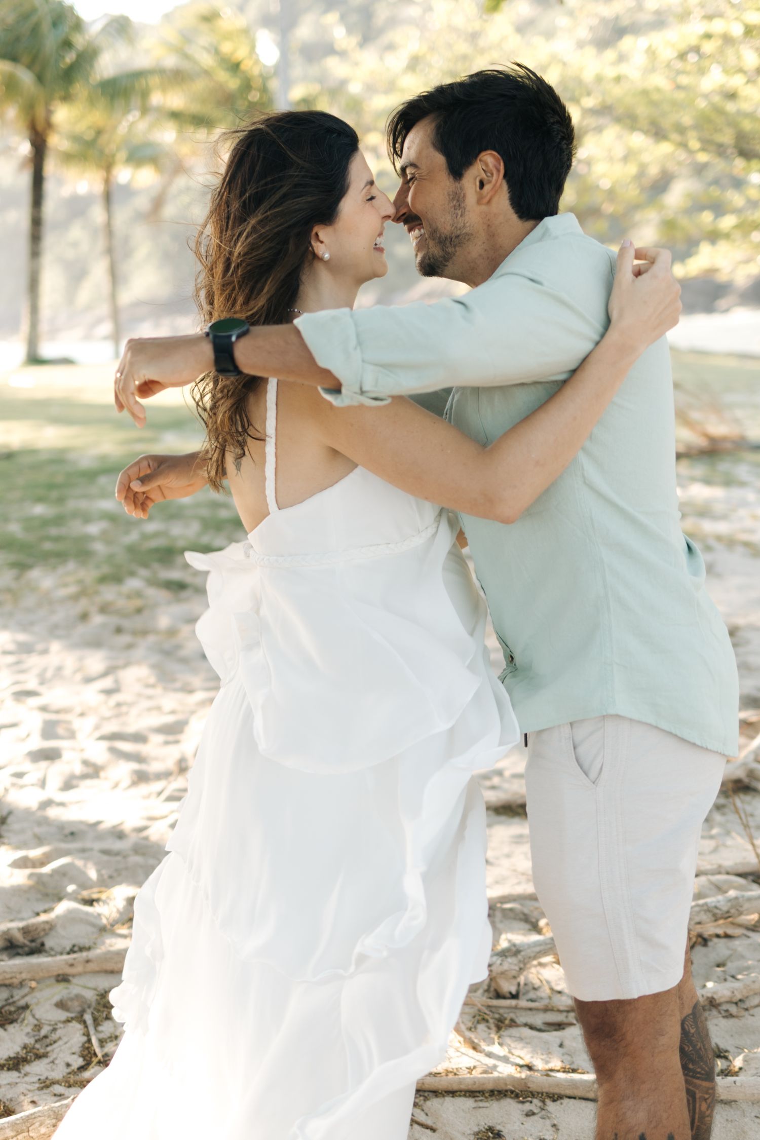 A joyful embrace between newlyweds on a beach with palm trees in the background.