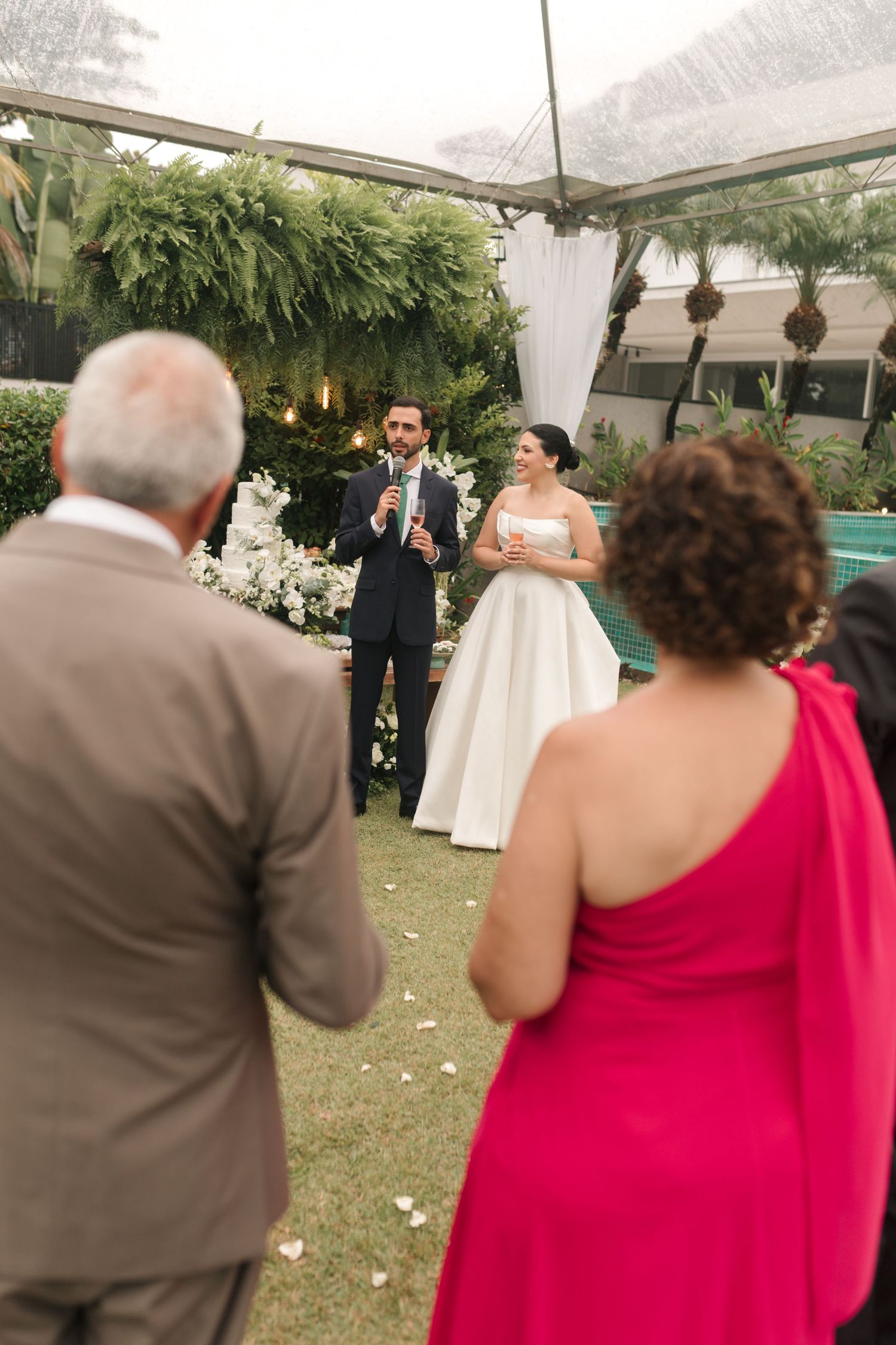 Wedding reception speech under a tent with hanging greenery and white decor.