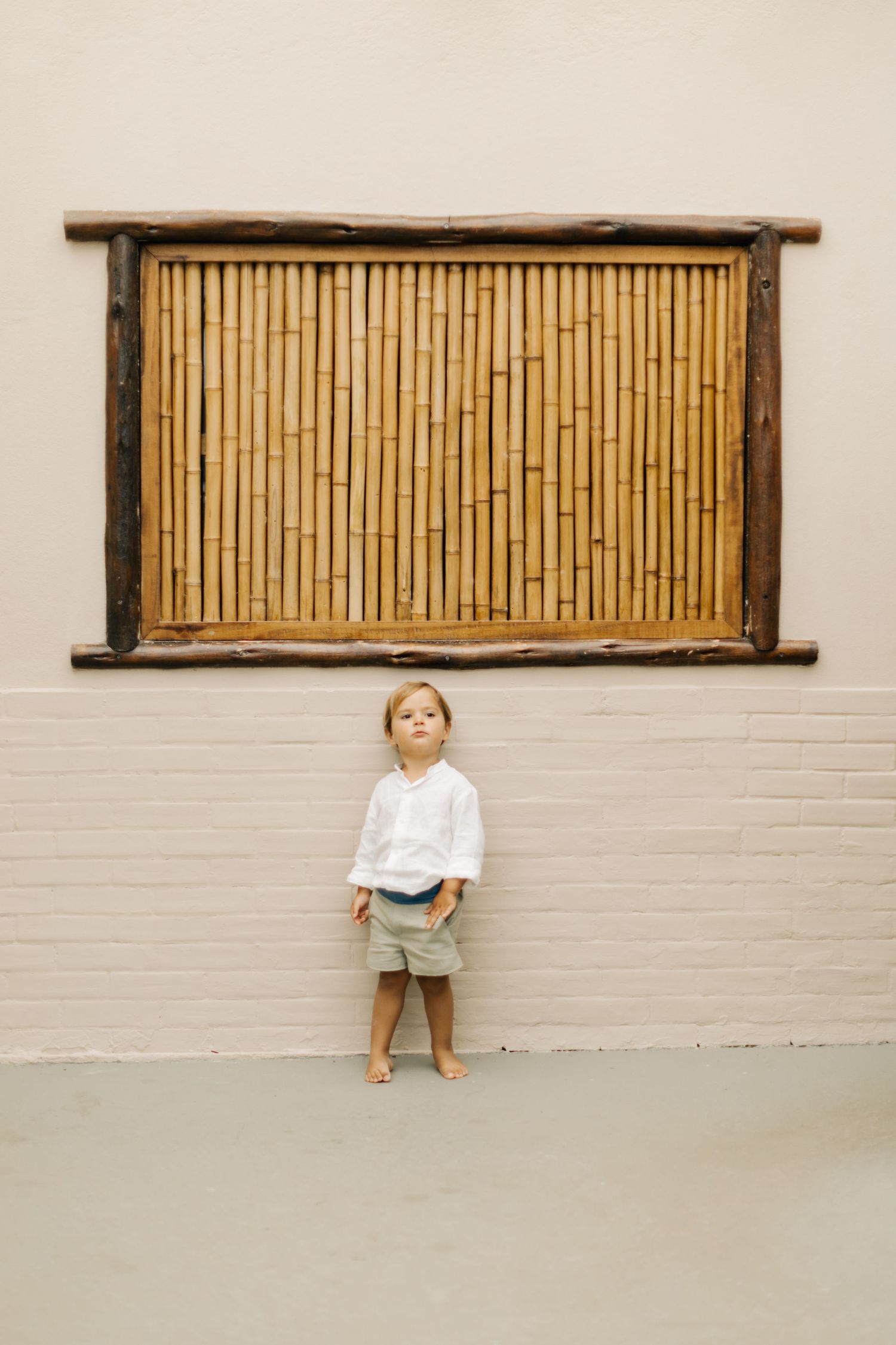 Small child standing against a wall with a bamboo decorative panel above.