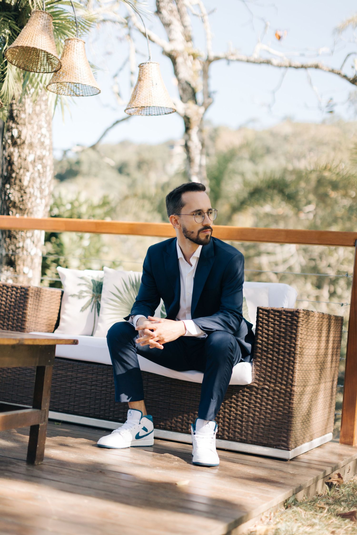 Man in navy suit relaxes on outdoor patio furniture with hanging bells in background.
