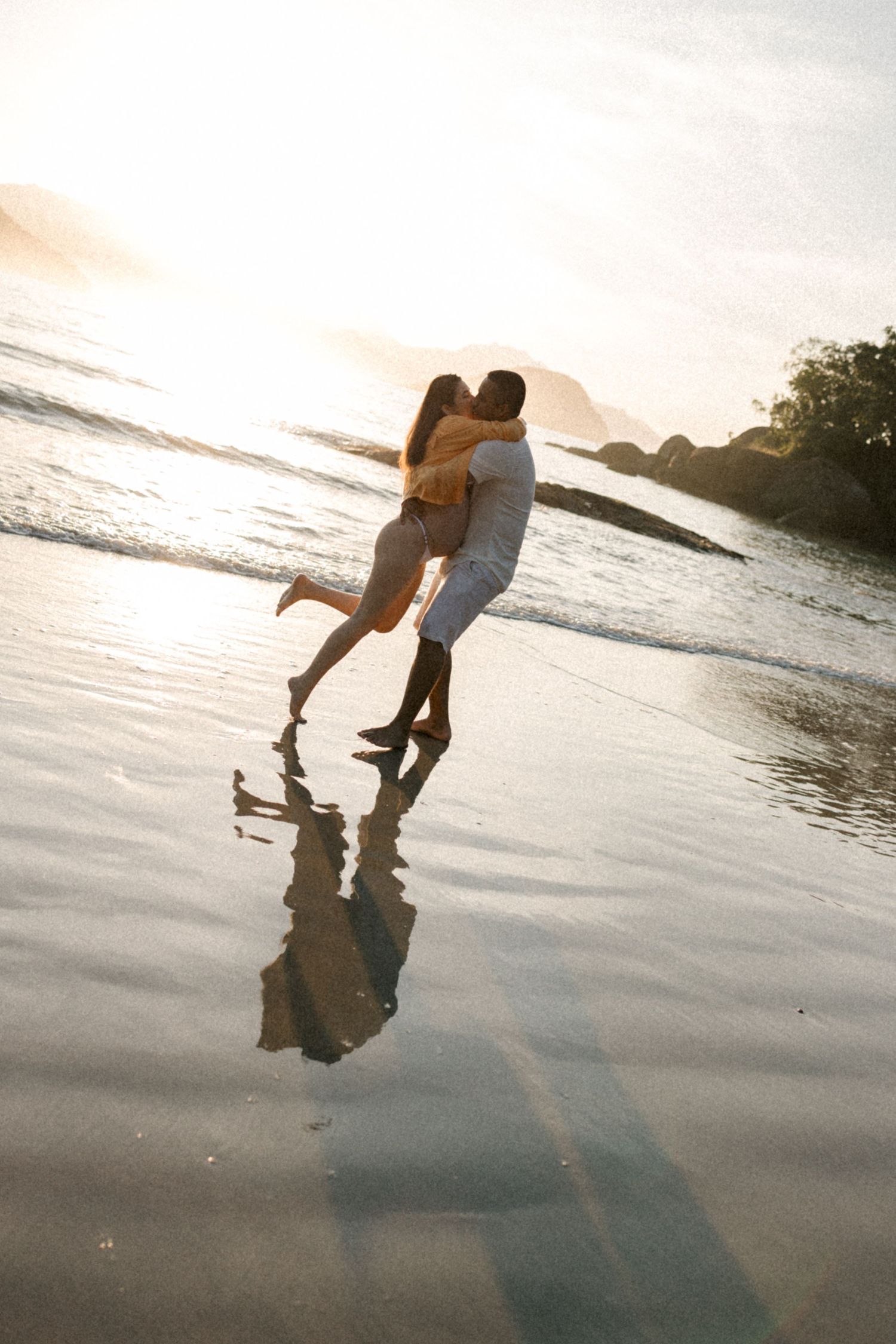 Couple creates romantic silhouette while dancing in shallow water at sunset on the beach.