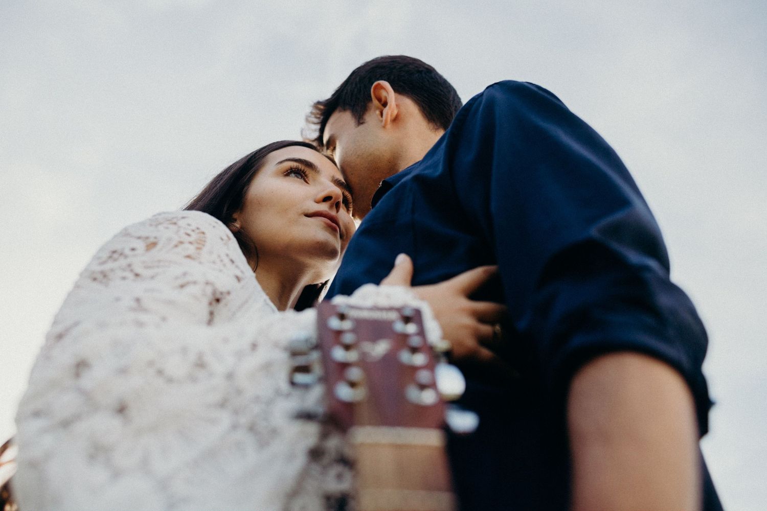 A romantic moment captured through guitar strings at sunset outdoors.