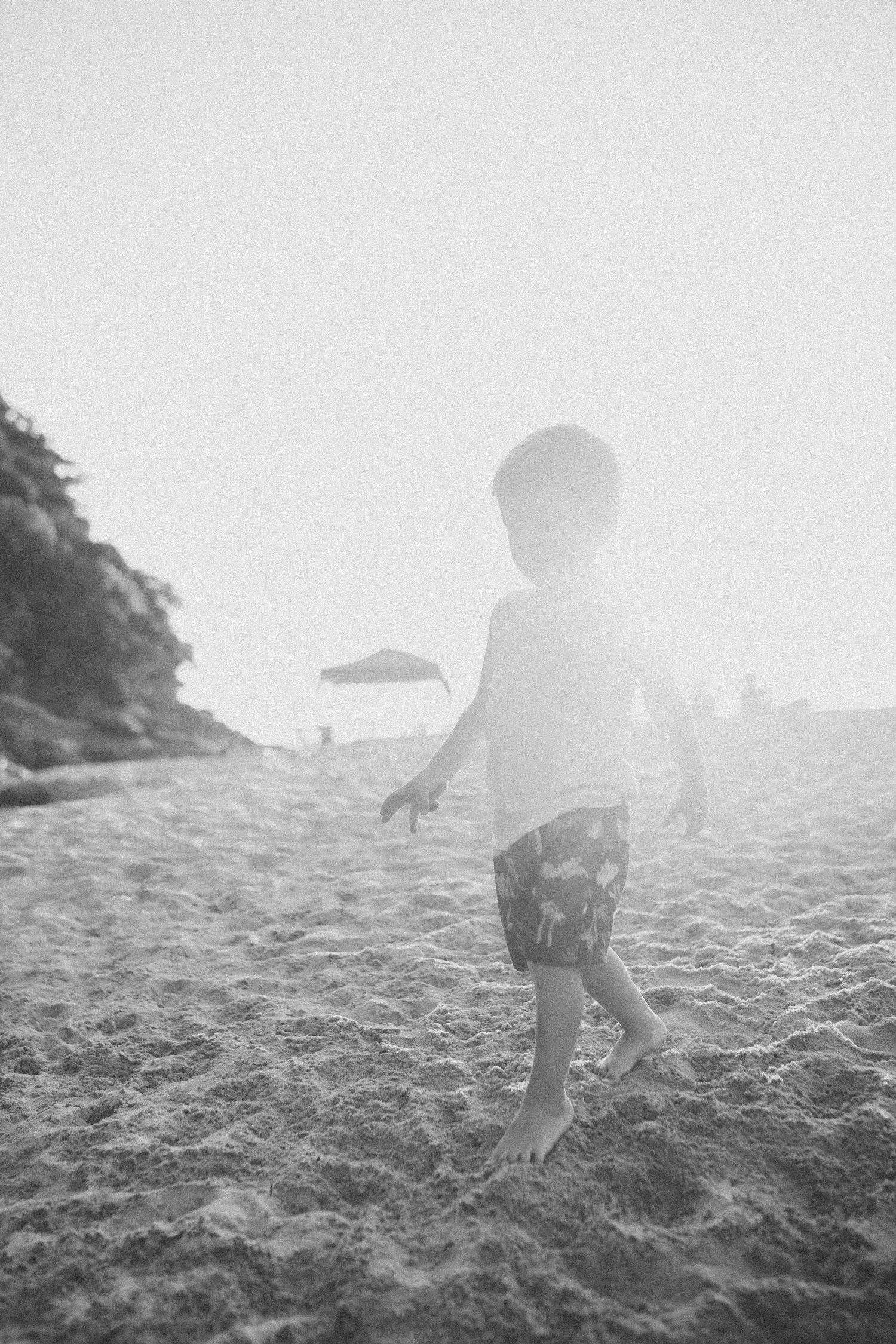 Silhouette of small child playing on sandy beach at sunset.