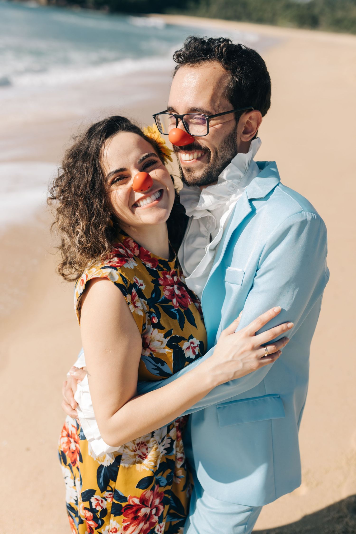 A joyful couple with red clown noses share a loving moment on a tropical beach.