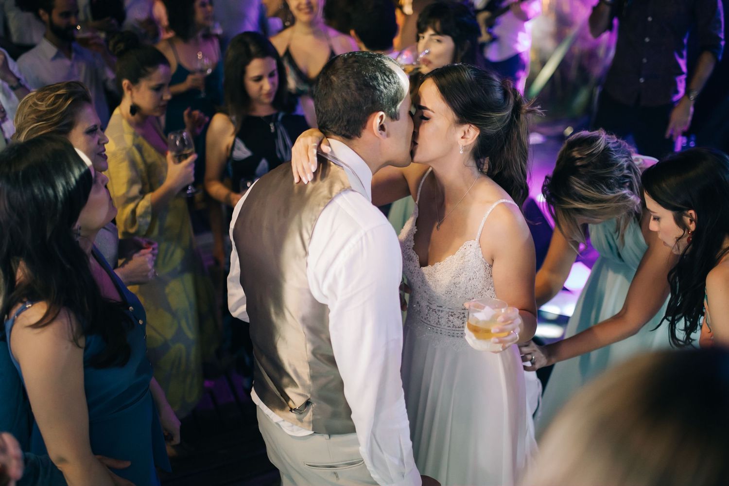 An intimate dance floor moment at a wedding reception with purple lighting and guests looking on.